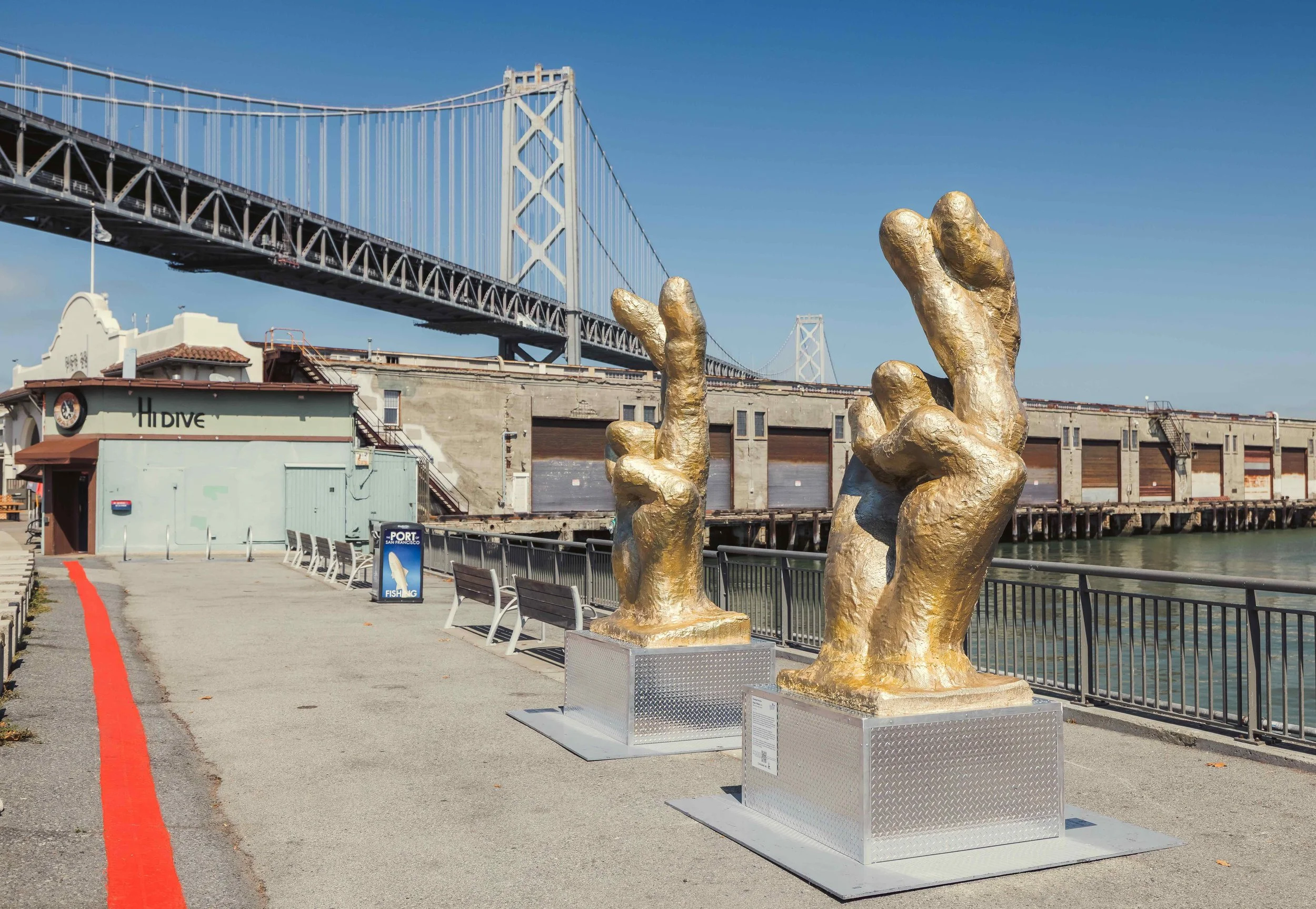 Two large sculptures of hands making peace signs with the Bay Bridge in the background