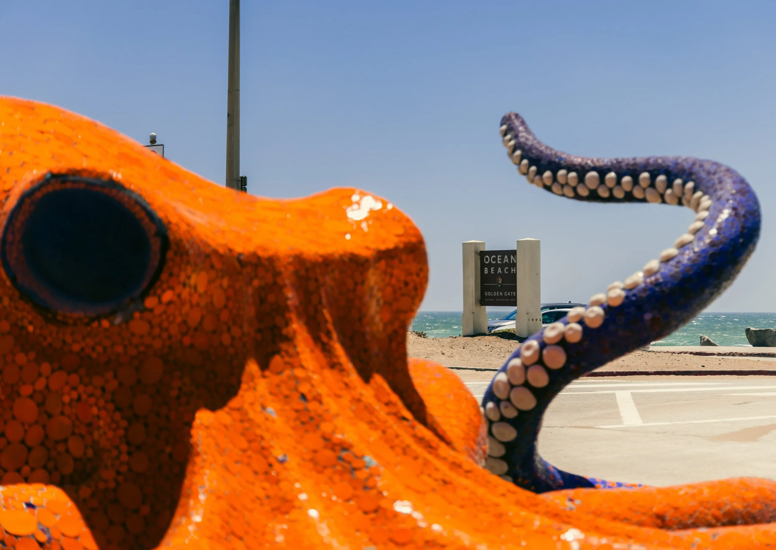 Colorful mosaic sculptures of a whale and an octopus at Ocean Beach, with a sign for Golden Gate National Recreation Area in the background.