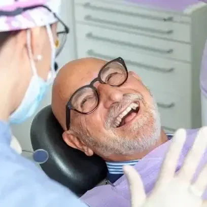 A smiling elderly man in a dental chair, wearing glasses and a dental bib, during a dental check-up with a dentist.