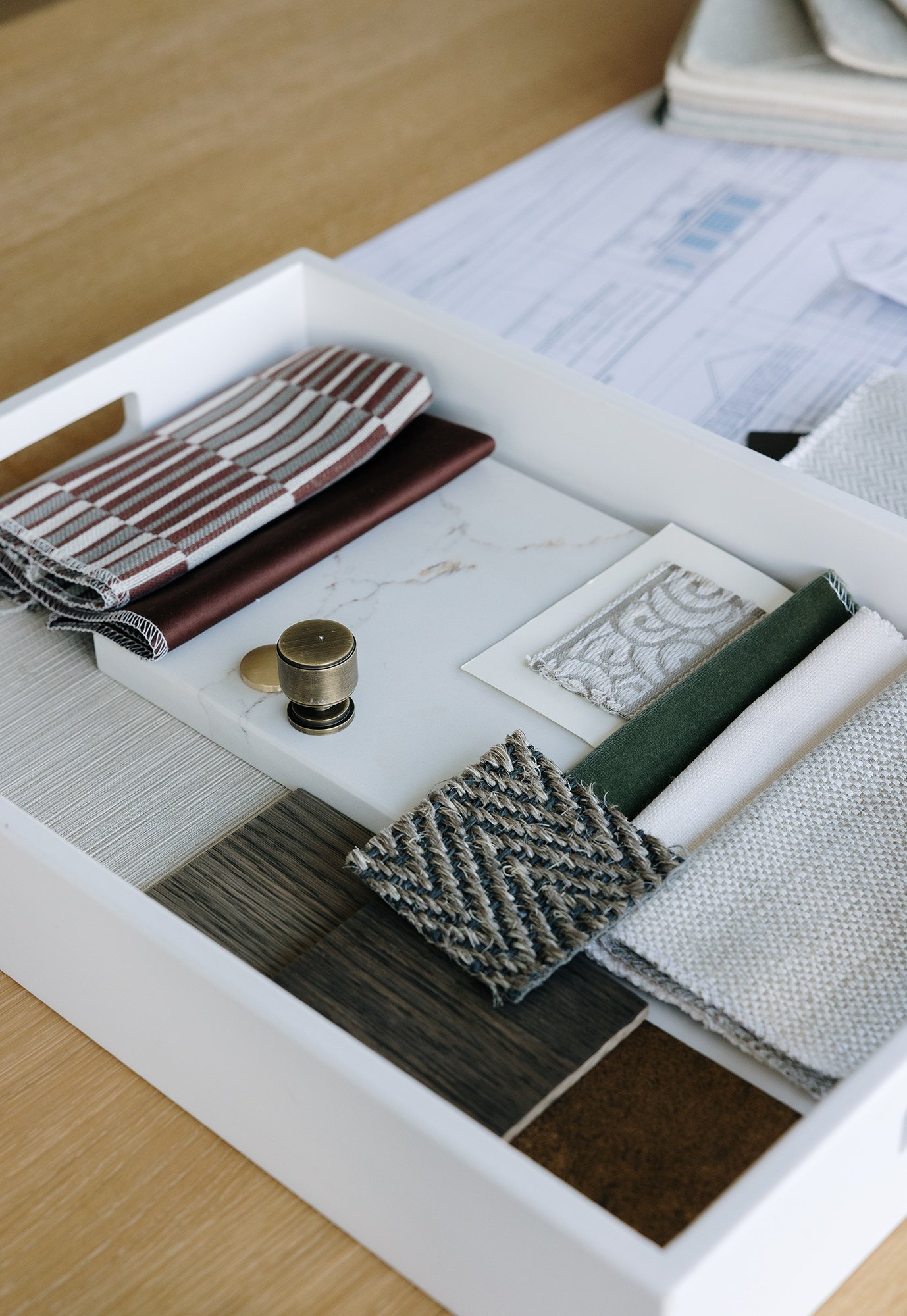 A sample book or fabric swatch collection with various fabric textures and colors, a small metal weight, and design sheets on a table.