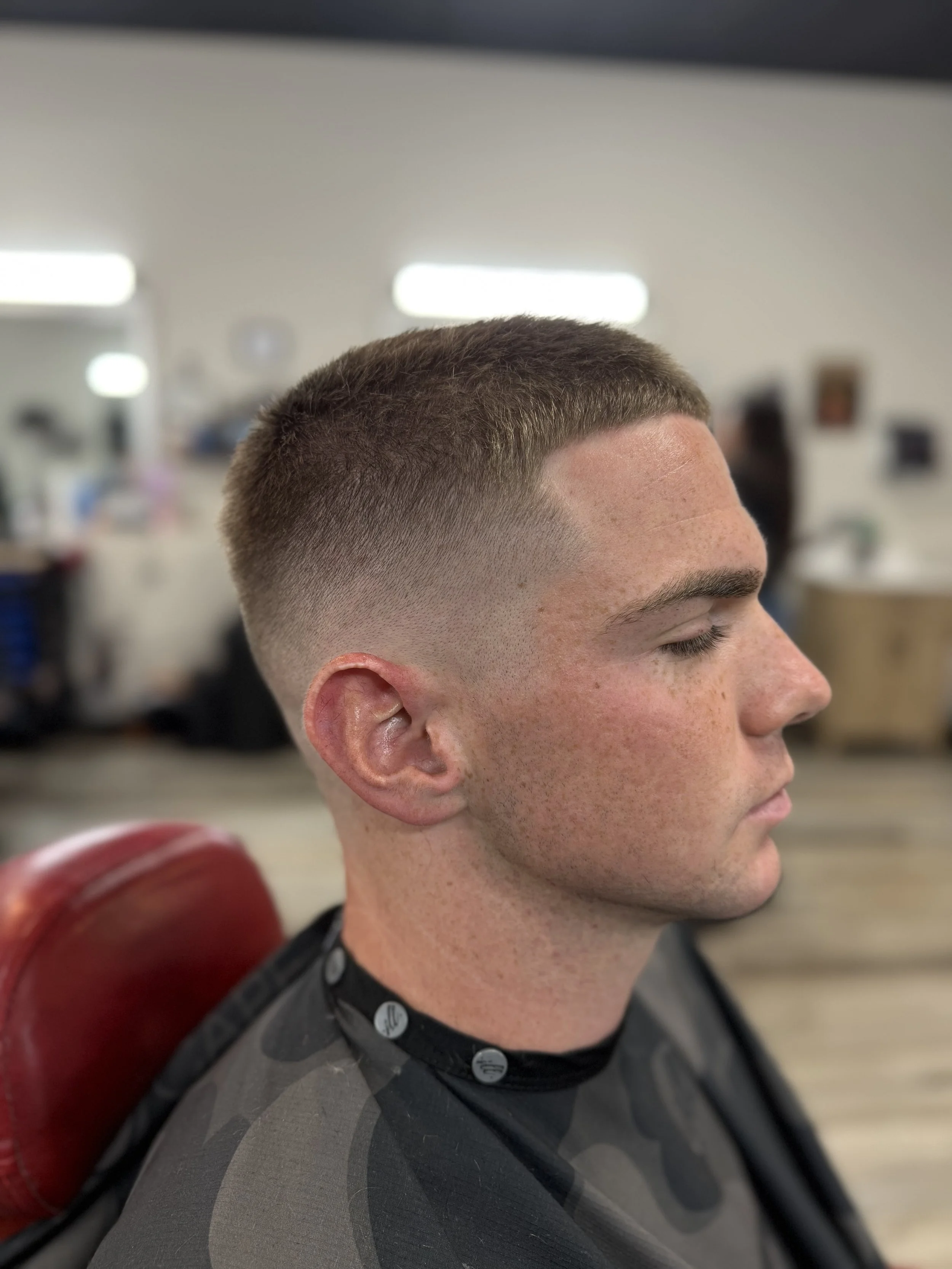 Side profile of a young man with a fresh, short fade haircut in a barbershop.