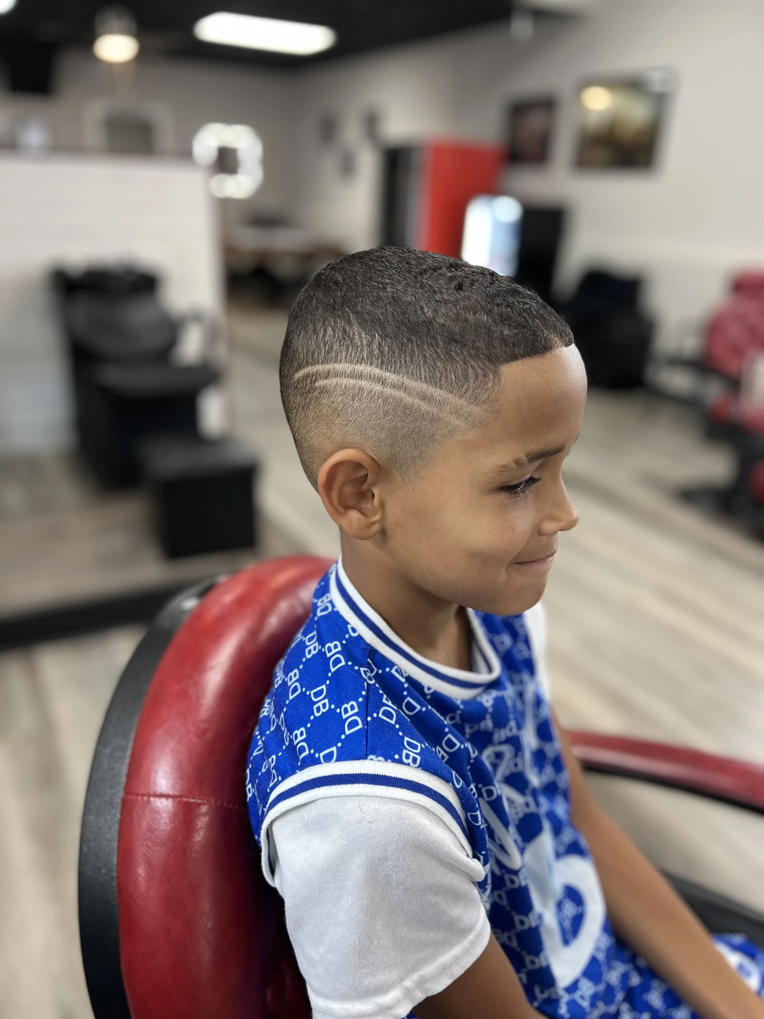 Young boy at a barber shop with a fresh, modern haircut featuring a fade and a curved line design.