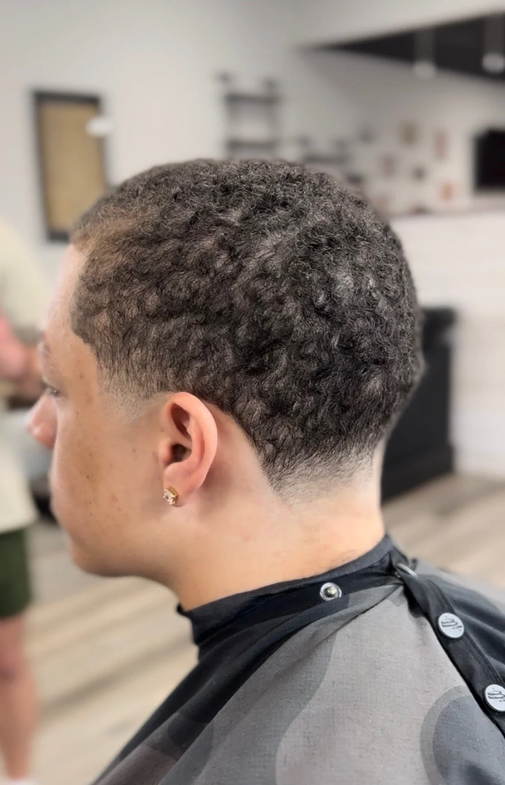 Close-up of a man with textured, curly hair and a fade haircut, sitting in a barber shop.