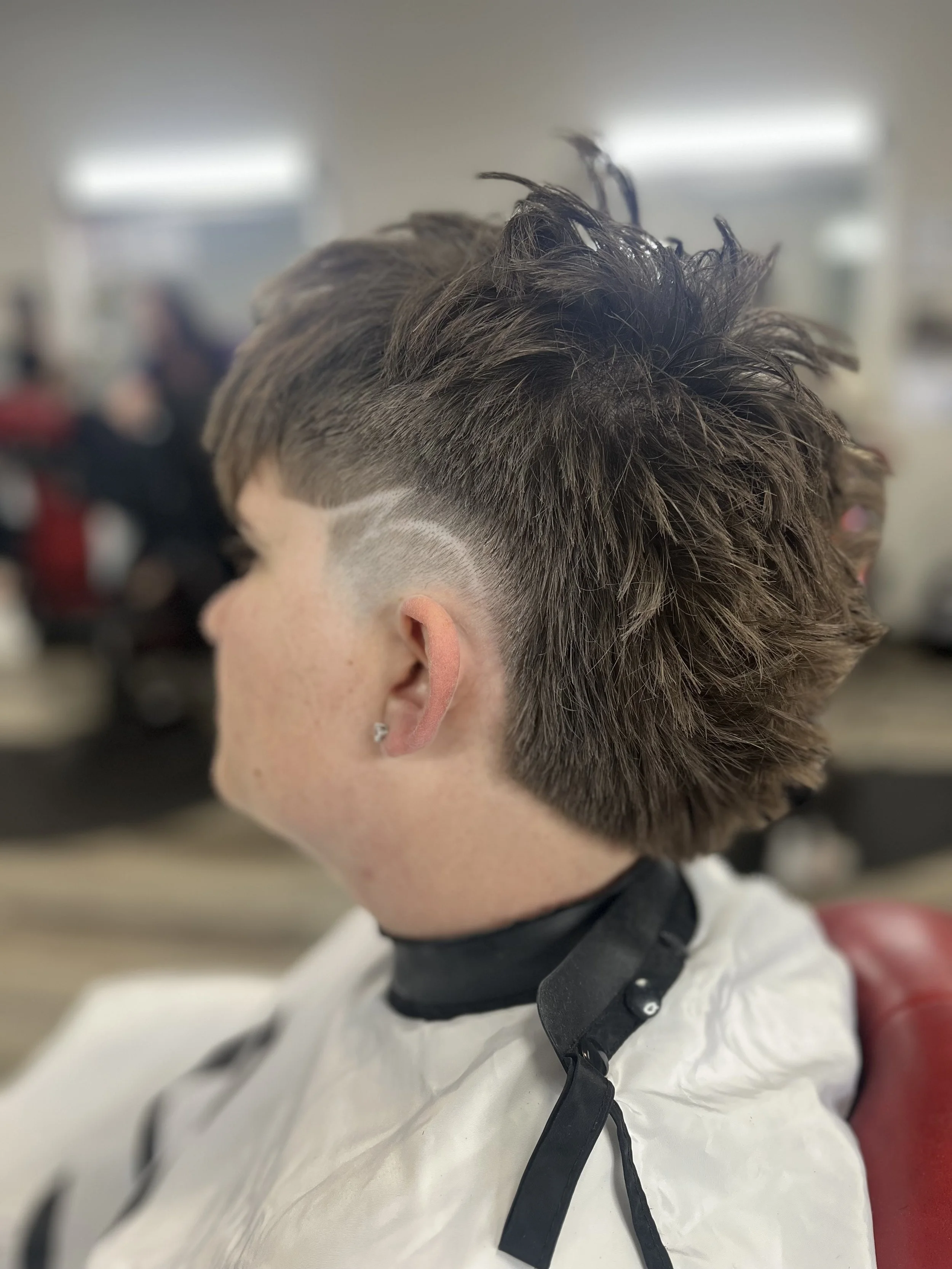 Close-up of a person with a new edgy hairstyle, featuring a fade on the sides and spiky, textured hair on top, sitting in a salon chair.