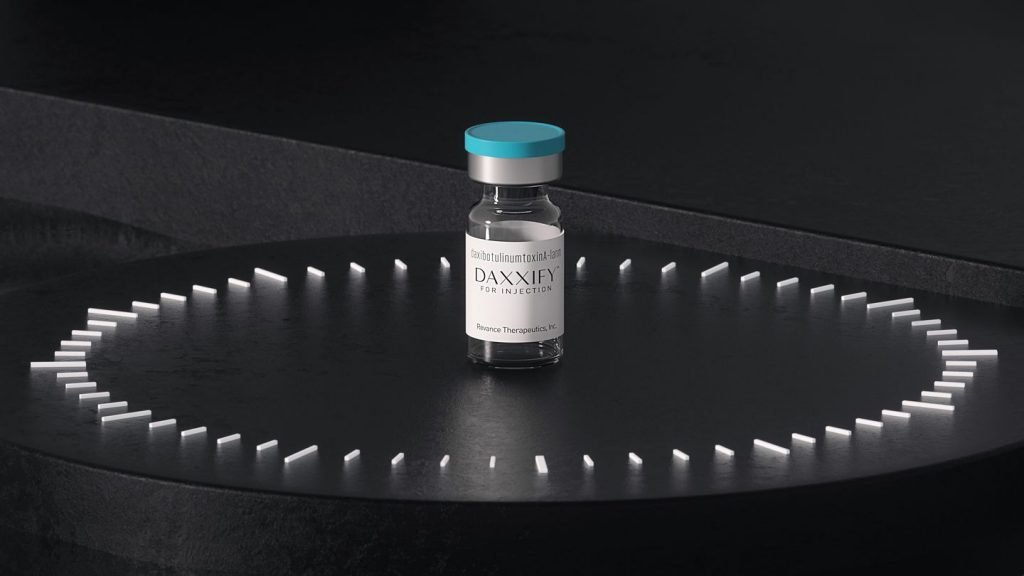 A vial labeled DAXXIFY on a black circular platform with white LED lights, against a dark background.
