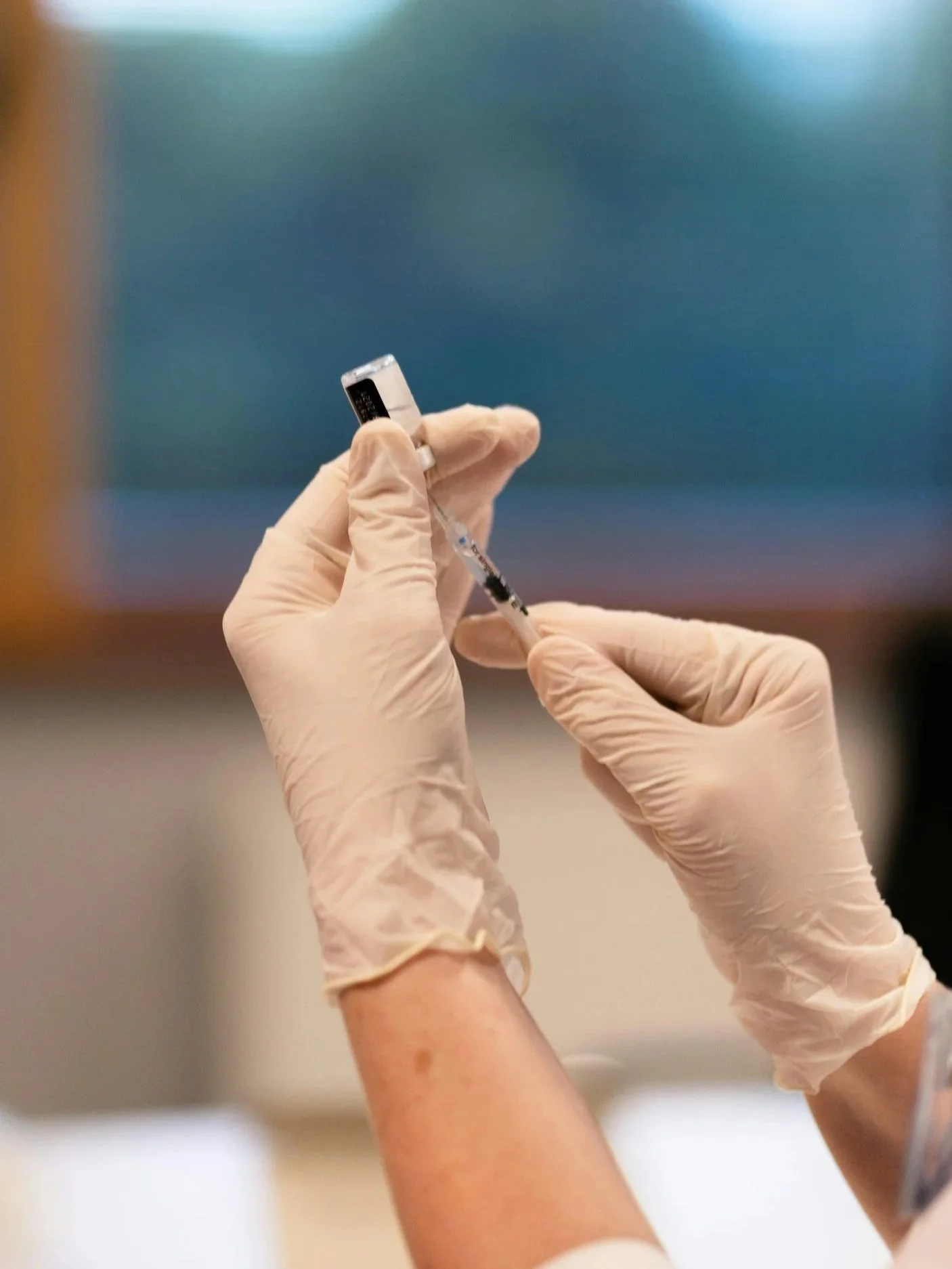 Person using gloved hands to prepare a syringe for medication.