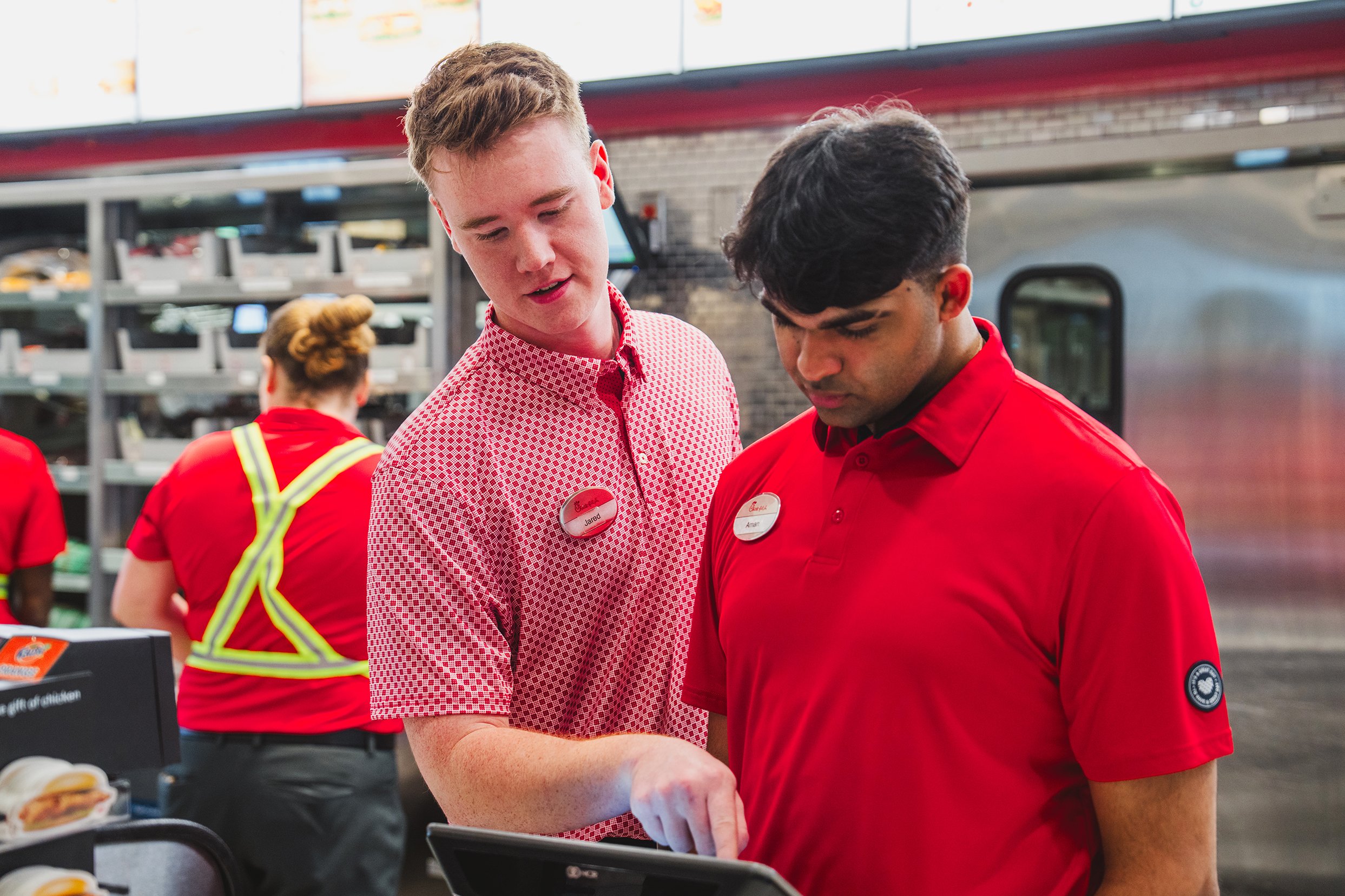 Two Chick-fil-A Nine Mile Road team members in red uniforms working together at the register inside the Pensacola restaurant.