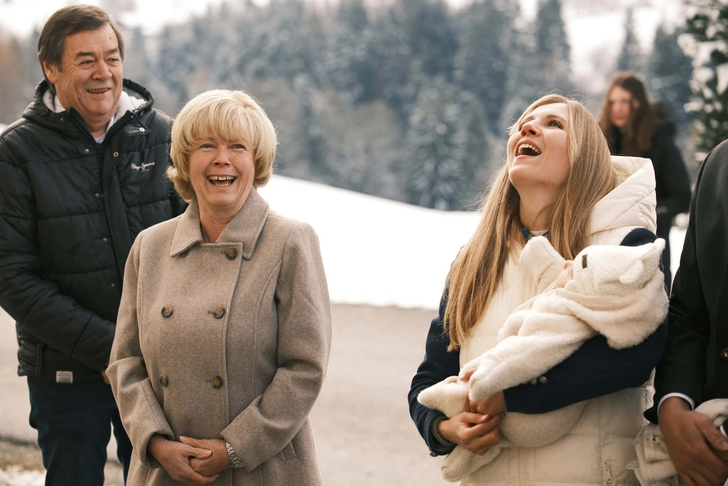 Mehrgenerationenfamilie im Winter im Freien, lachend und Spaß habend, im Hintergrund verschneite Bäume.