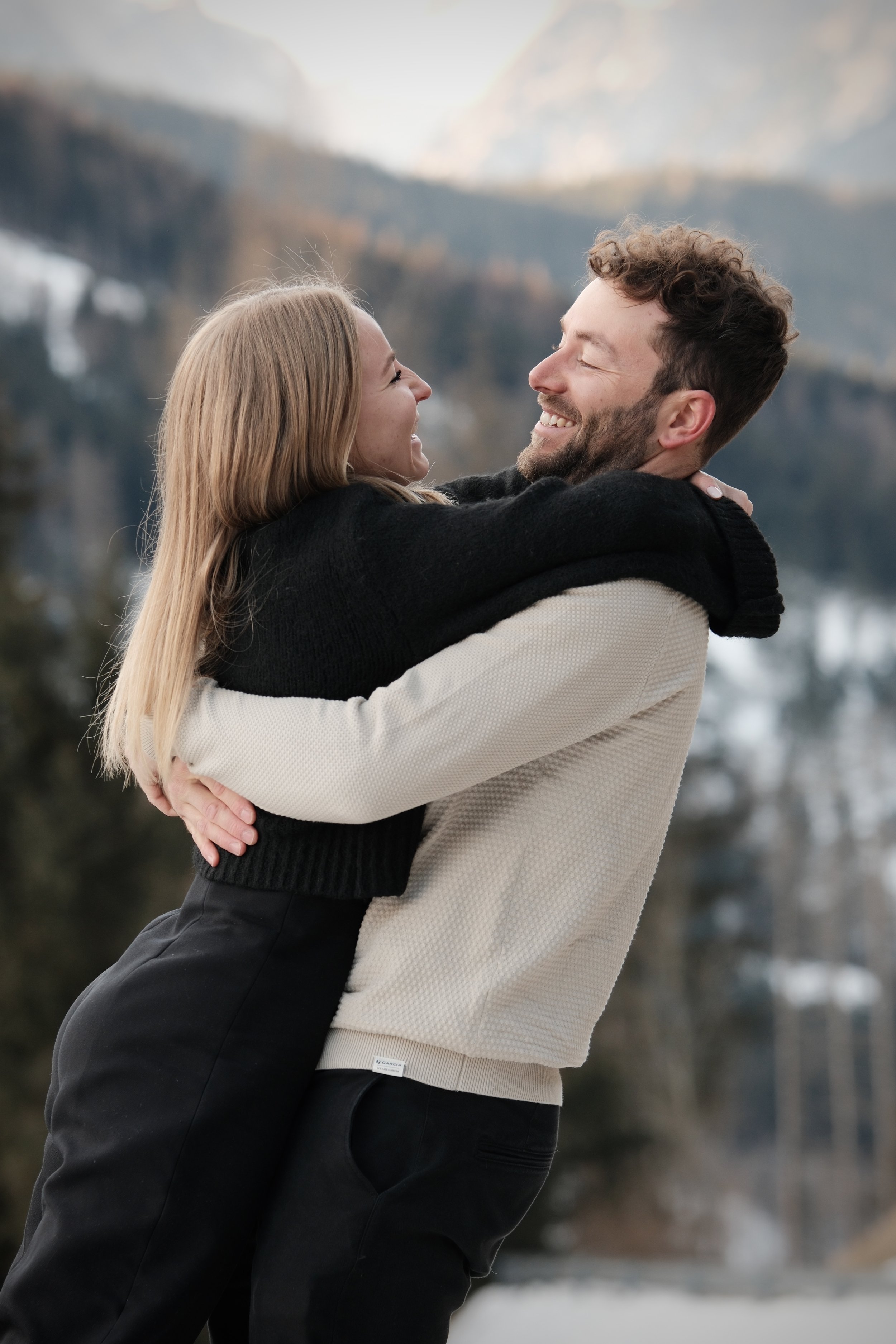 Ein glückliches Paar umarmt sich draußen vor einer bergigen Landschaft.