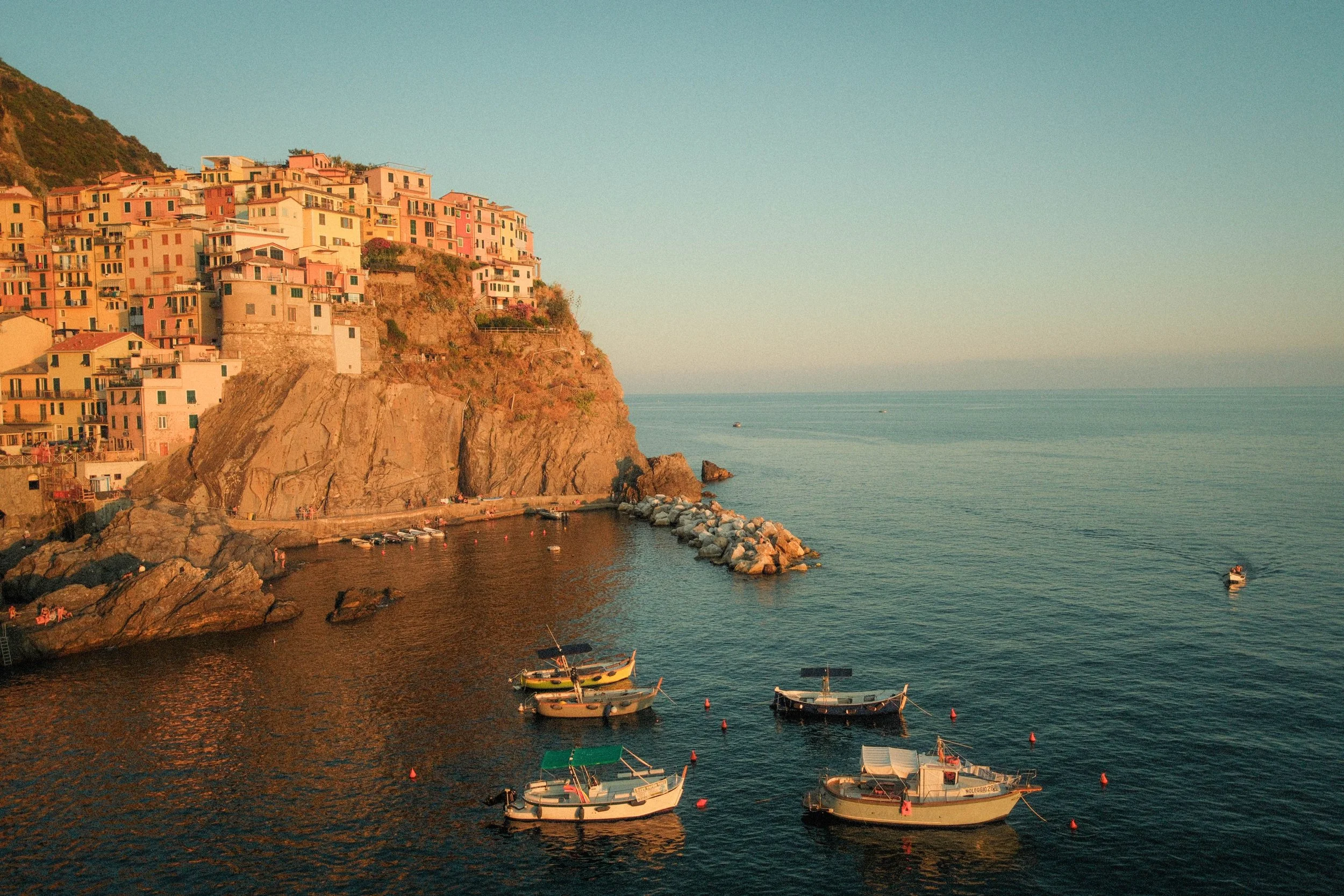 Bunte Häuser auf einer Klippe, mit Booten im Wasser vor der Küste bei Sonnenuntergang, Italien