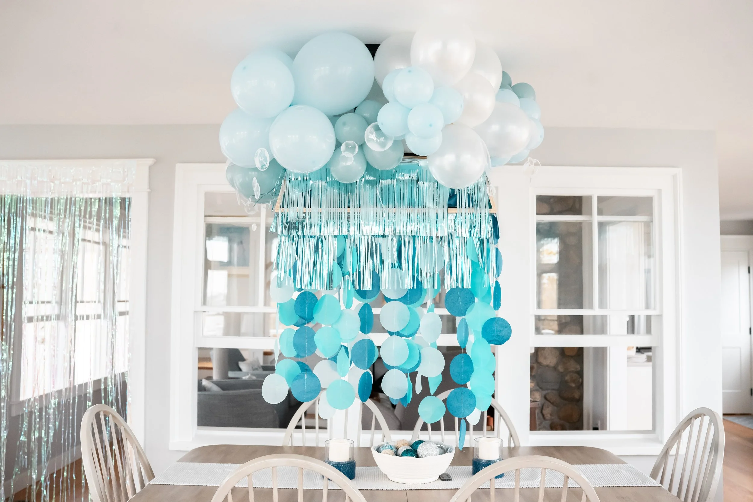 Blue and white balloon garland hanging above a dining table with candles and a bowl of decorative balls in the center of the table.