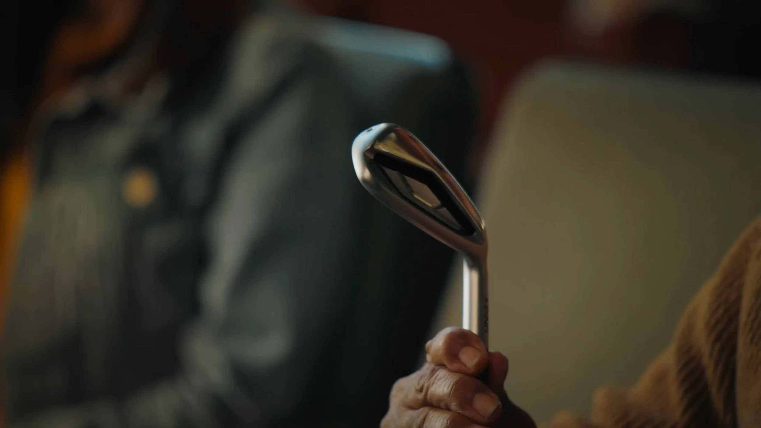 From Chariot's advertisement with PING, a golf club company. Close-up of a person's hand holding a shiny golf club, with other golf clubs blurred in the background.