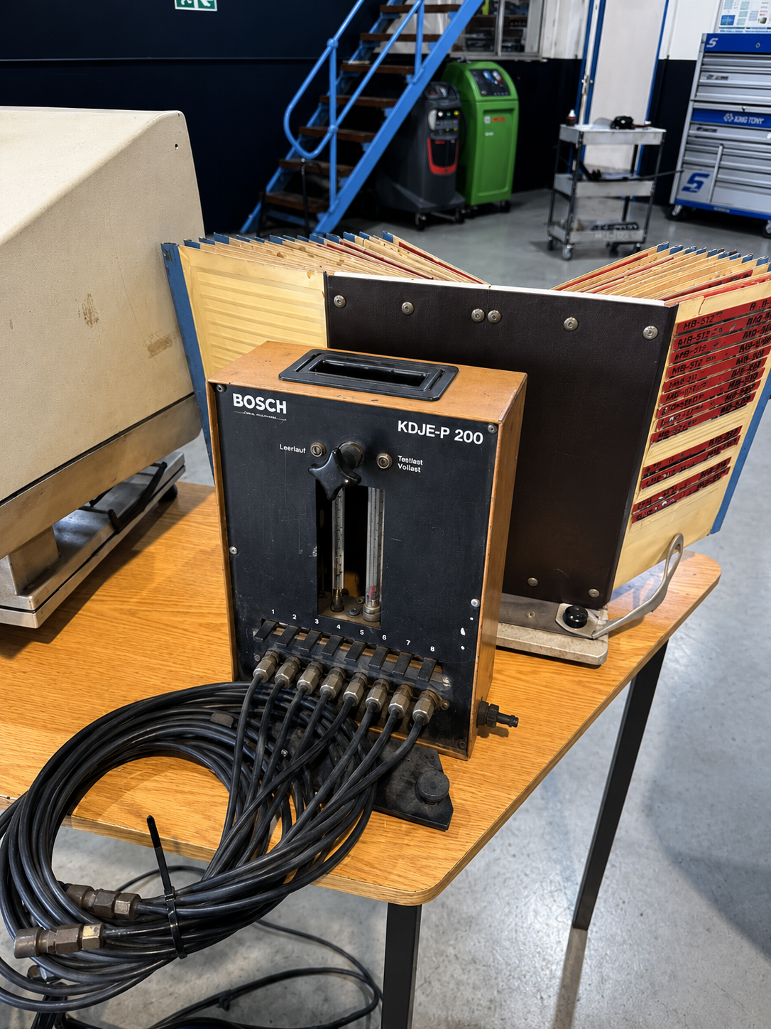 A U-shaped industrial testing device with multiple cables connected at the bottom, labeled BOSCH KDJE-P 200, placed on a wooden table in a workshop.