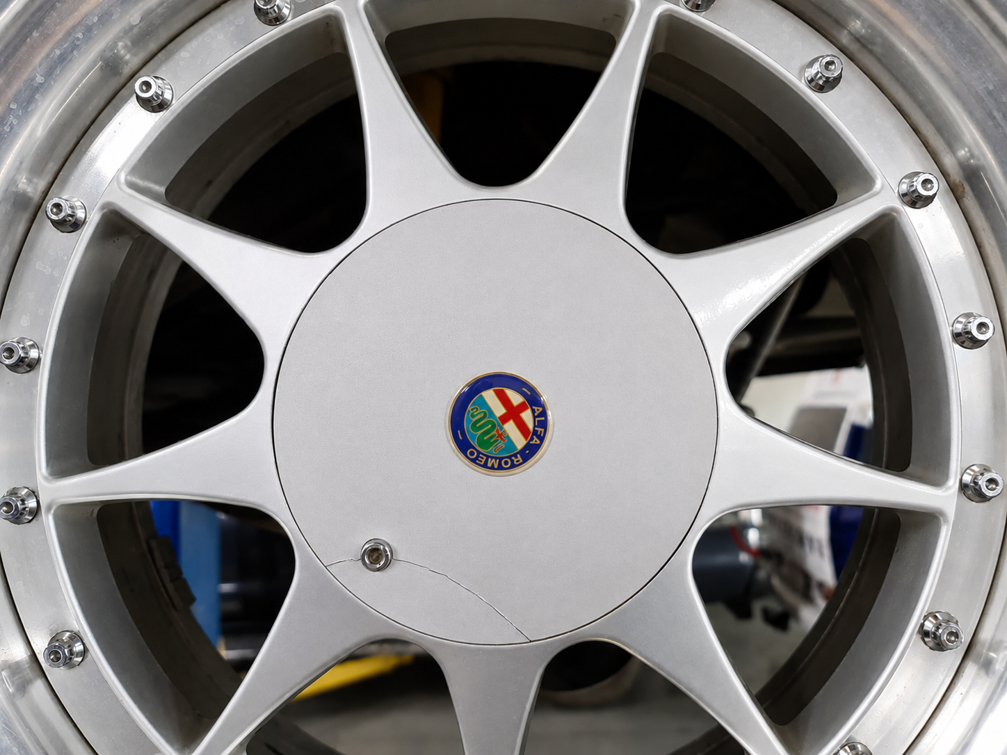 Close-up of a silver Alfa Romeo racing wheel with a center cap featuring the Alfa Romeo logo, mounted on a car.