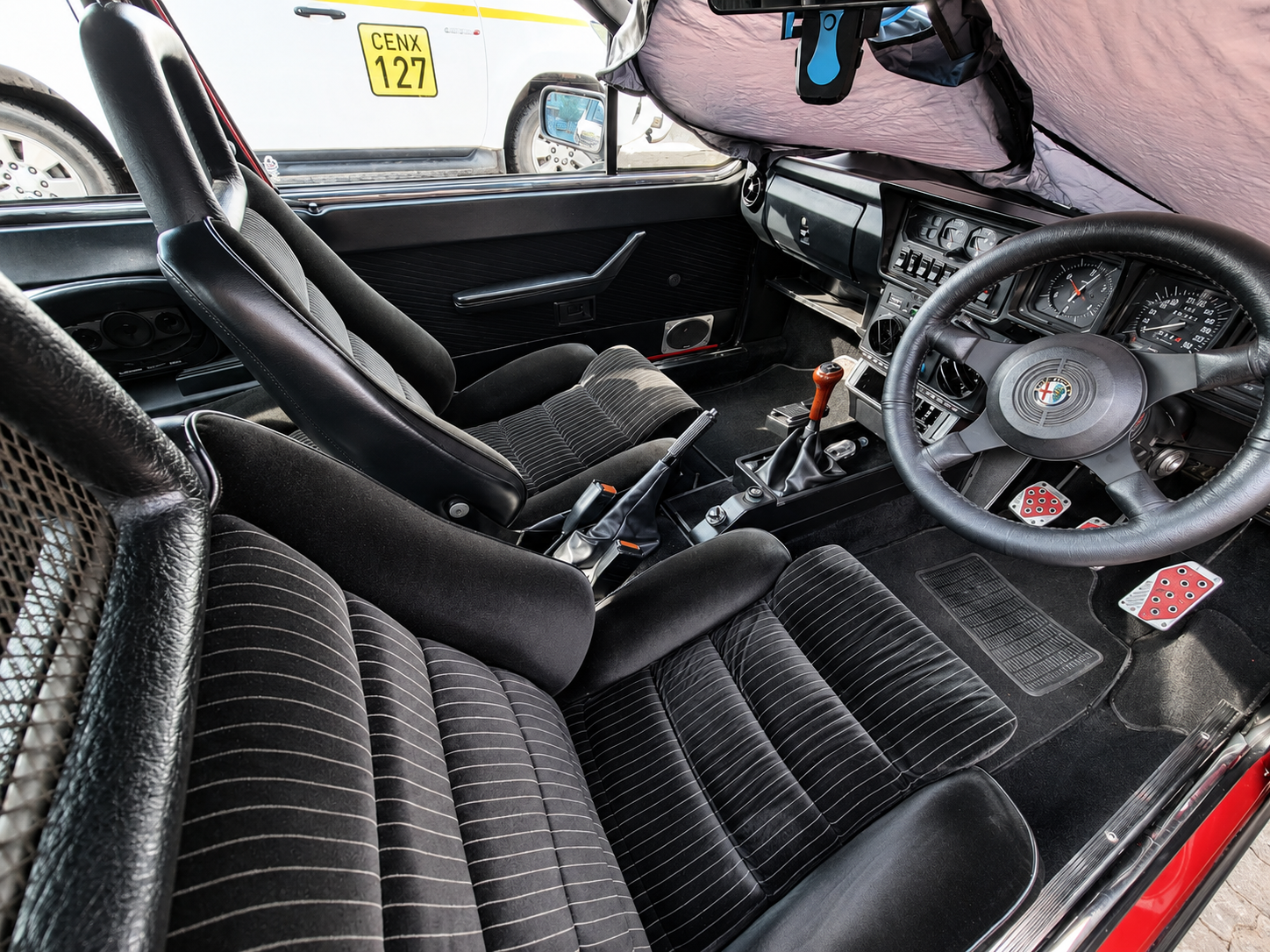Interior of a classic Alfa Romeo car with black seats, a steering wheel, gear shift, and dashboard with various gauges.
