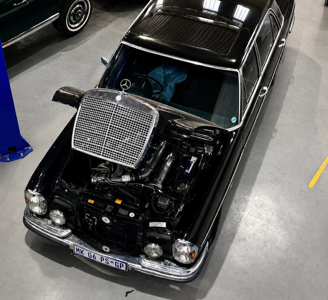 A black classic Mercedes-Benz with an exposed engine and a large radiator cover, parked indoors on a gray concrete floor.