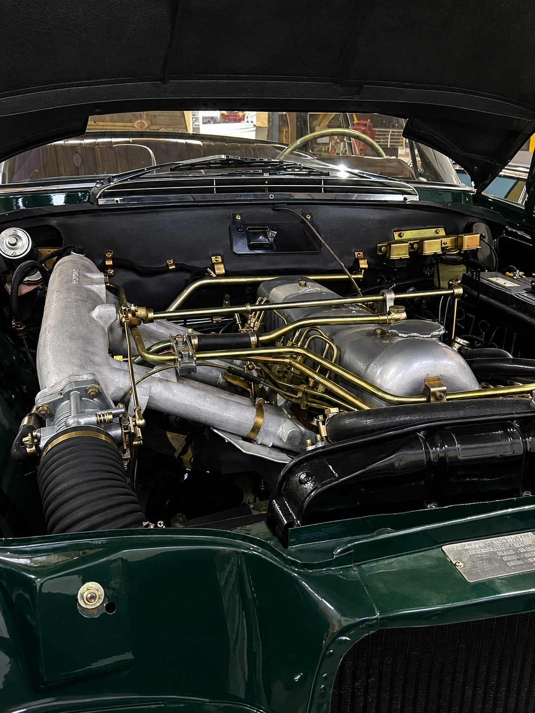 Close-up of a vintage car engine with gold-colored parts, silver valve covers, and black hoses in a classic car showroom.