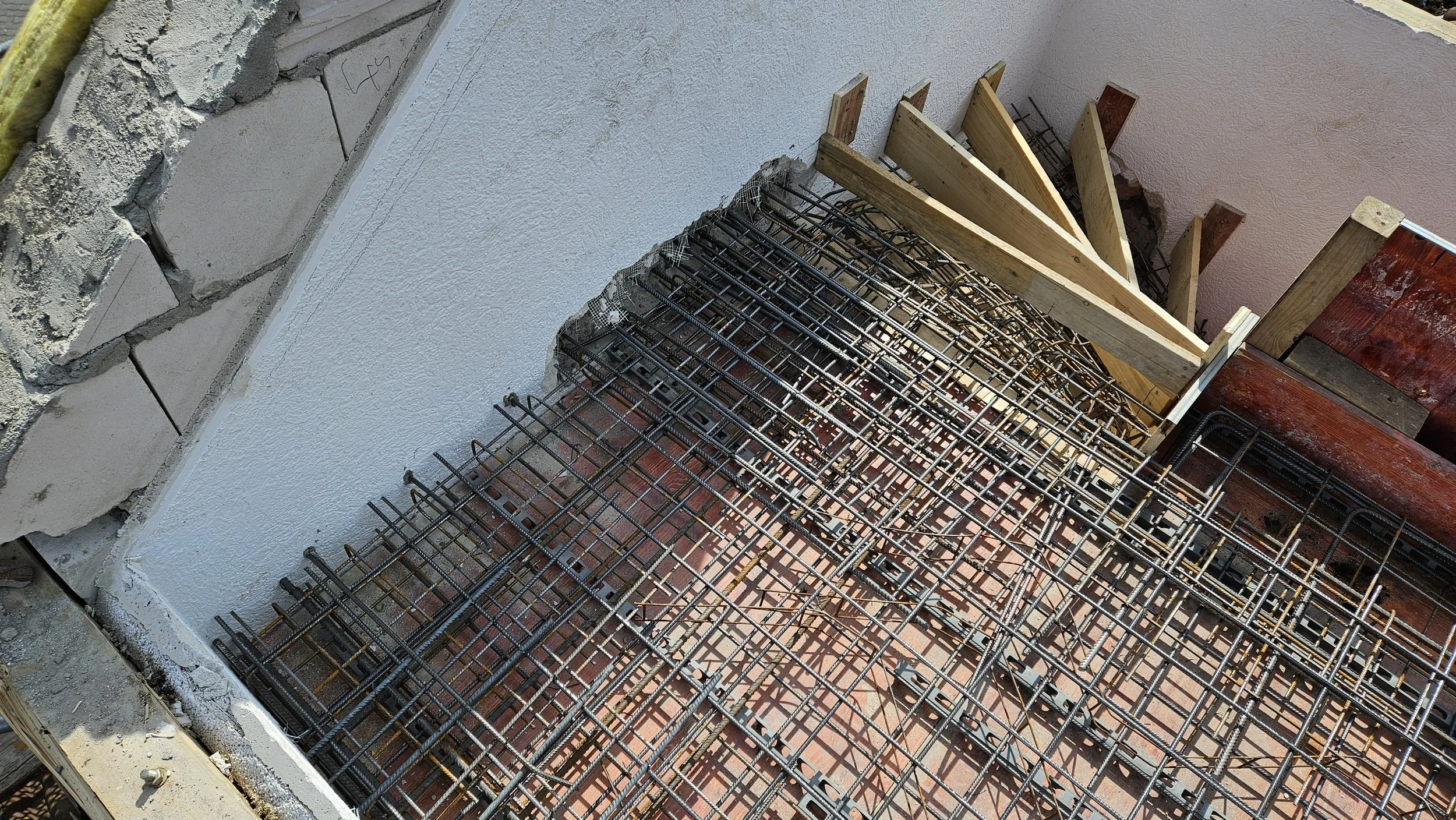 Blick auf eine Baustelle mit Stahlbewehrung, Holzverschalungen und rotem Stahlträger, der für einen Betoniereinbau vorbereitet wird.