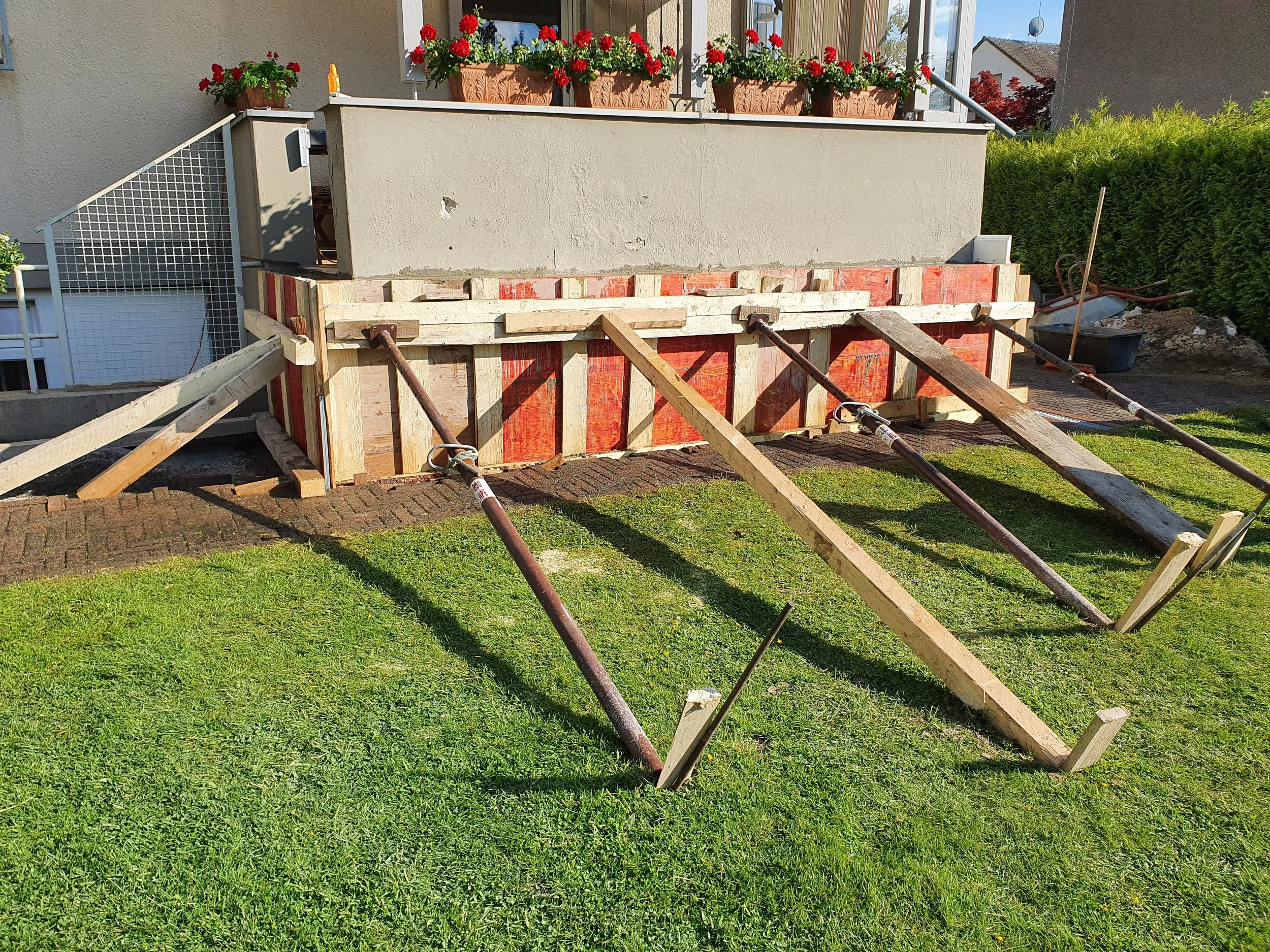 Bauarbeiten an einer Hausfassade mit Gerüst und Holzkonstruktion im Garten.