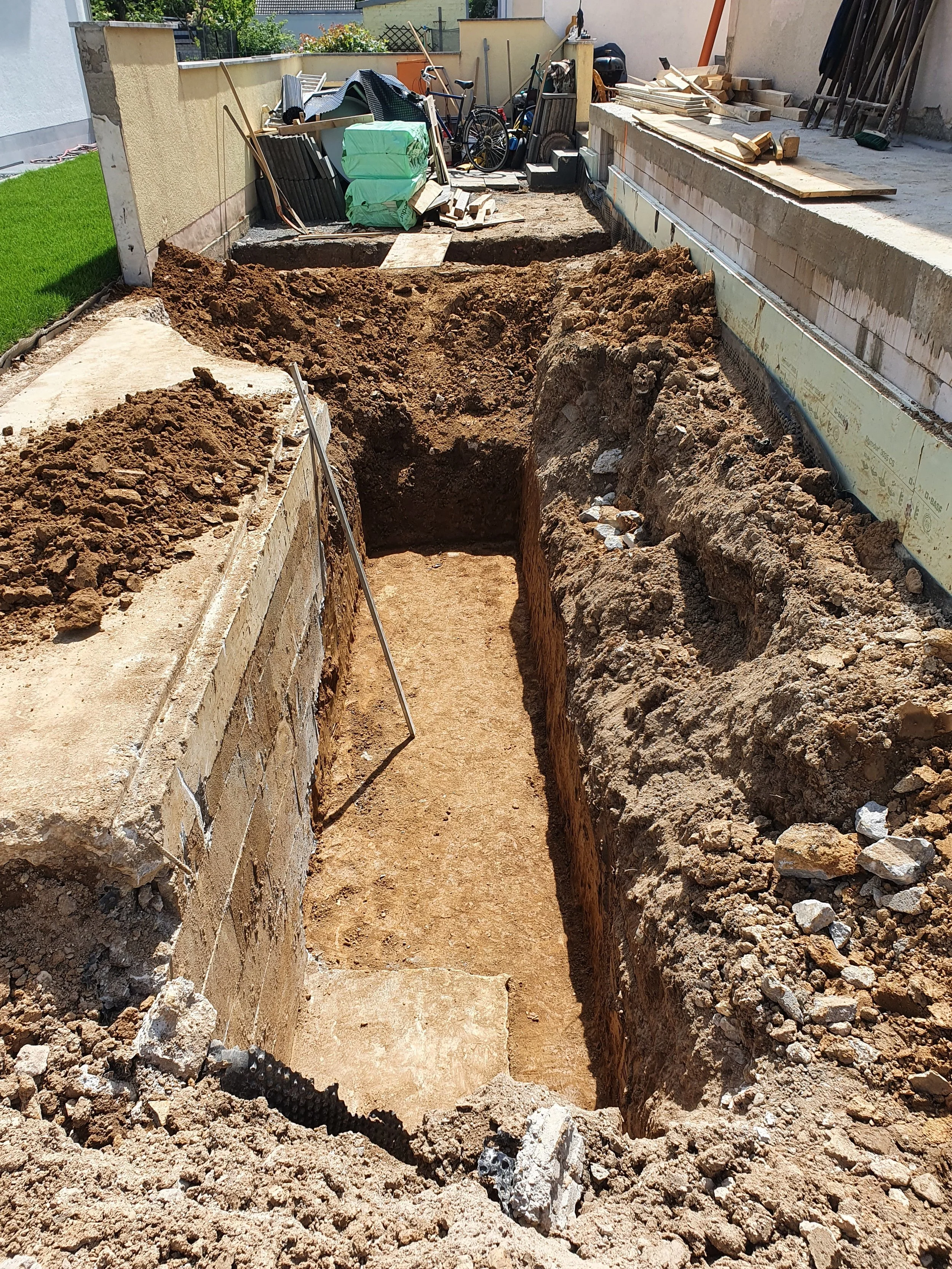 A construction site with a trench dug in the ground, surrounded by building materials, tools, and equipment for foundation work.