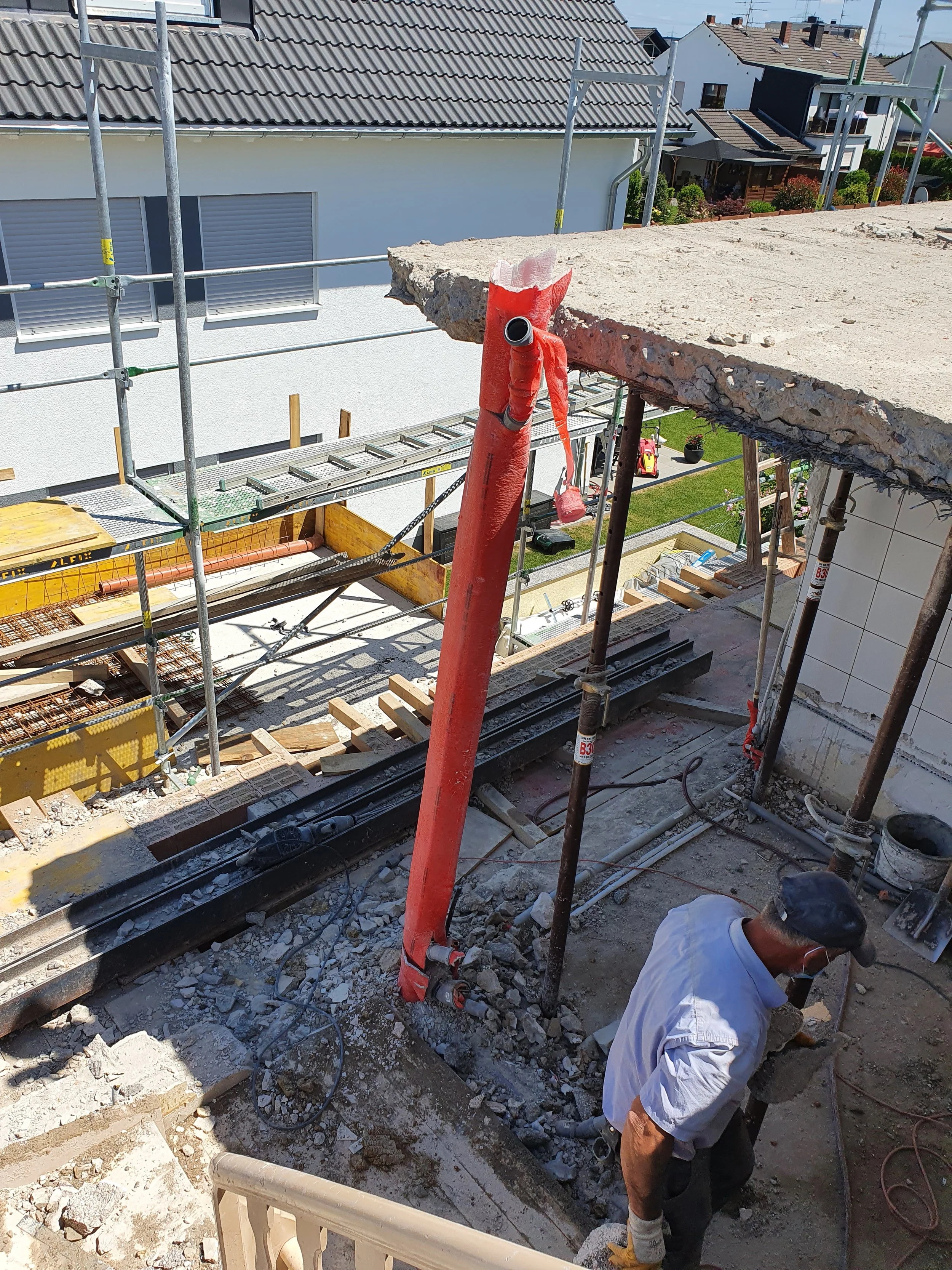 Bauarbeiter arbeitet auf einer Baustelle mit Gerüst und schwerem Betonstück auf einem Balkon. Das Bild zeigt den Baufortschritt eines Gebäudes.