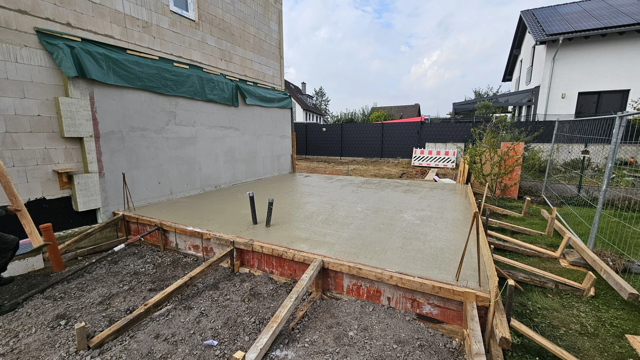 Letzter Schritt der Betoneindeckung im Garten, im Hintergrund Nachbarhäuser, Bauzaun und Garten.
