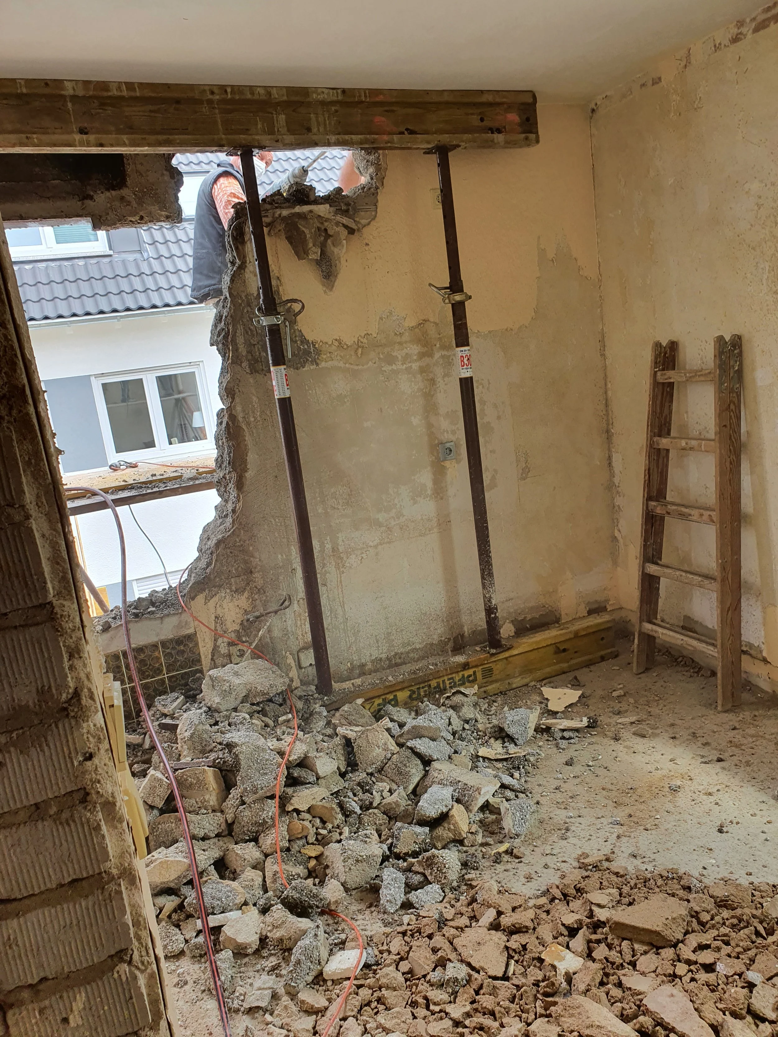 Renovierungsarbeiten in einem Raum mit einer großen Wandöffnung, Baugerüst, Steinen und Werkzeugen.