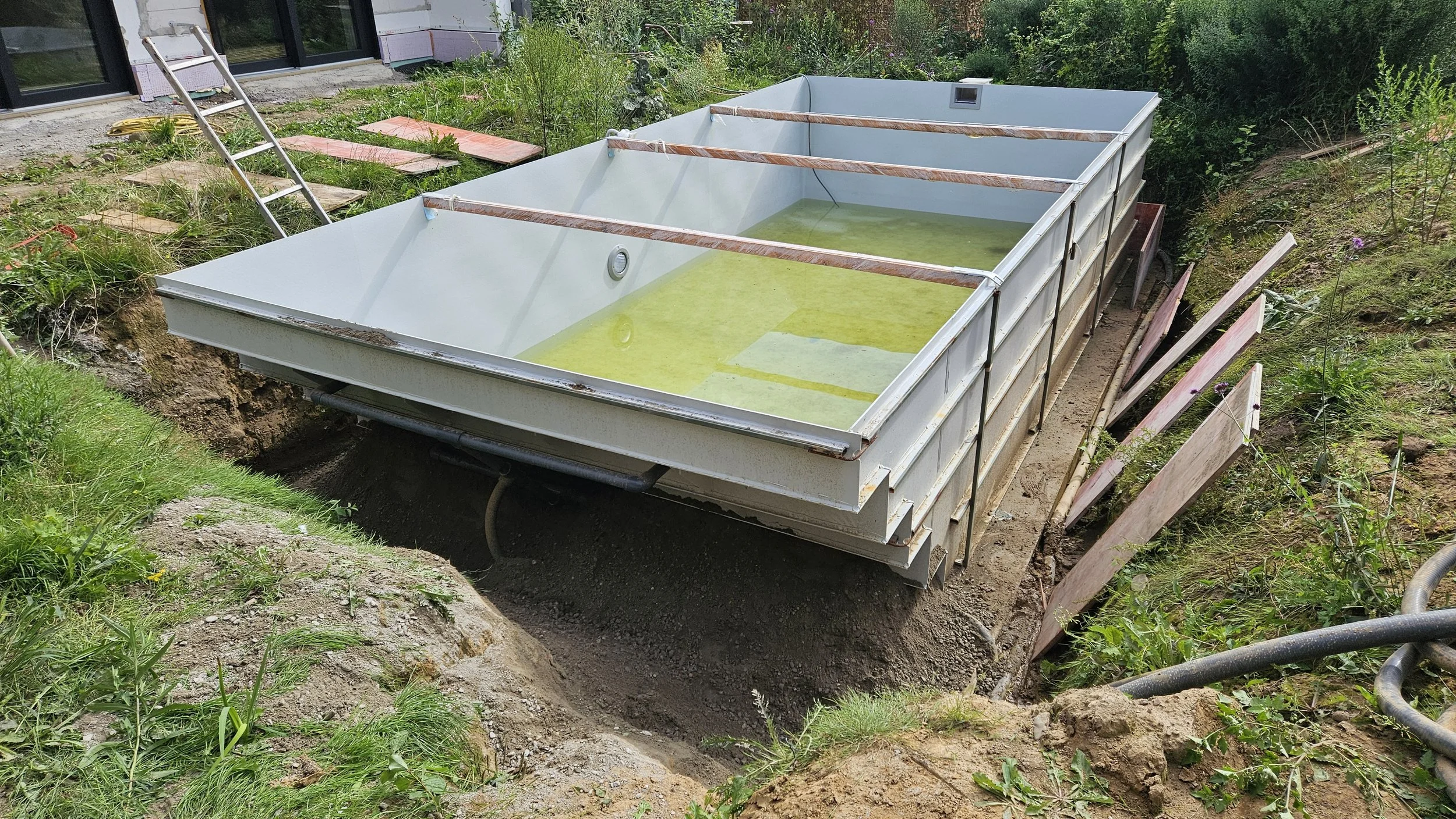 Bau einer großen Wasserbecken oder Teich im Garten, eingebettet in Erde, umgeben von Pflanzen und Baustoffen.