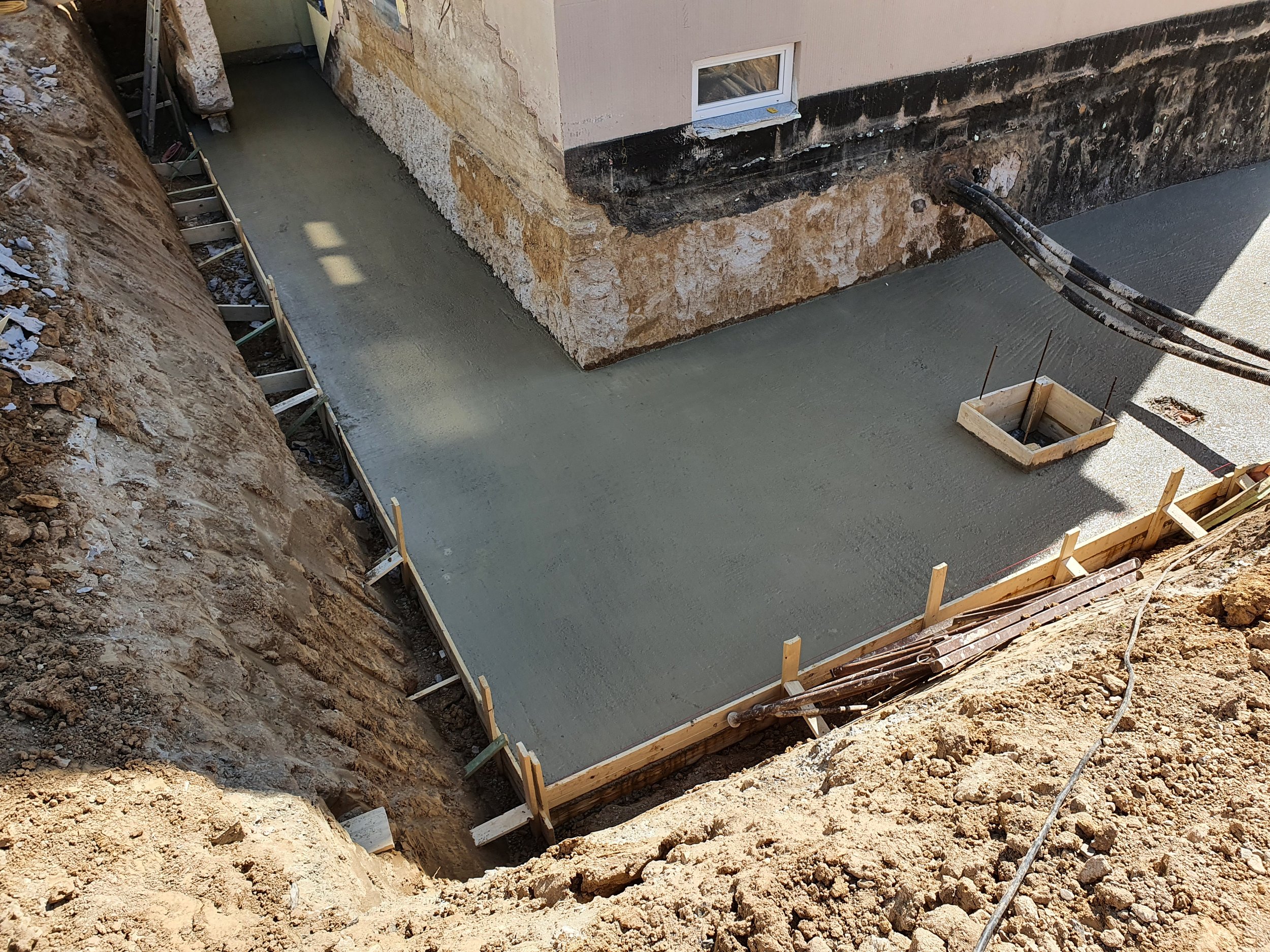 Betonfundament für den Bau eines Hauses, umgeben von Erdarbeiten, mit Holz Rahmen und Kabel auf der Baustelle.