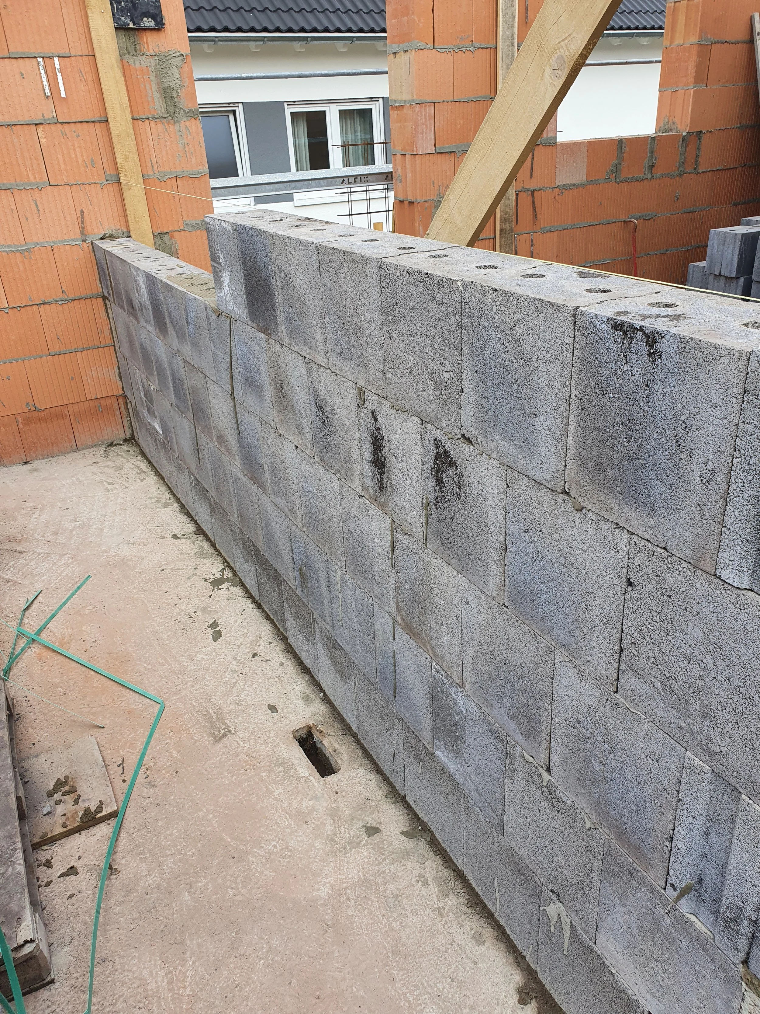 Eine Baustelle mit einer Mauer aus grauen Steinblöcken. Im Hintergrund sind Häuser mit weißen und grauen Fassaden sichtbar.