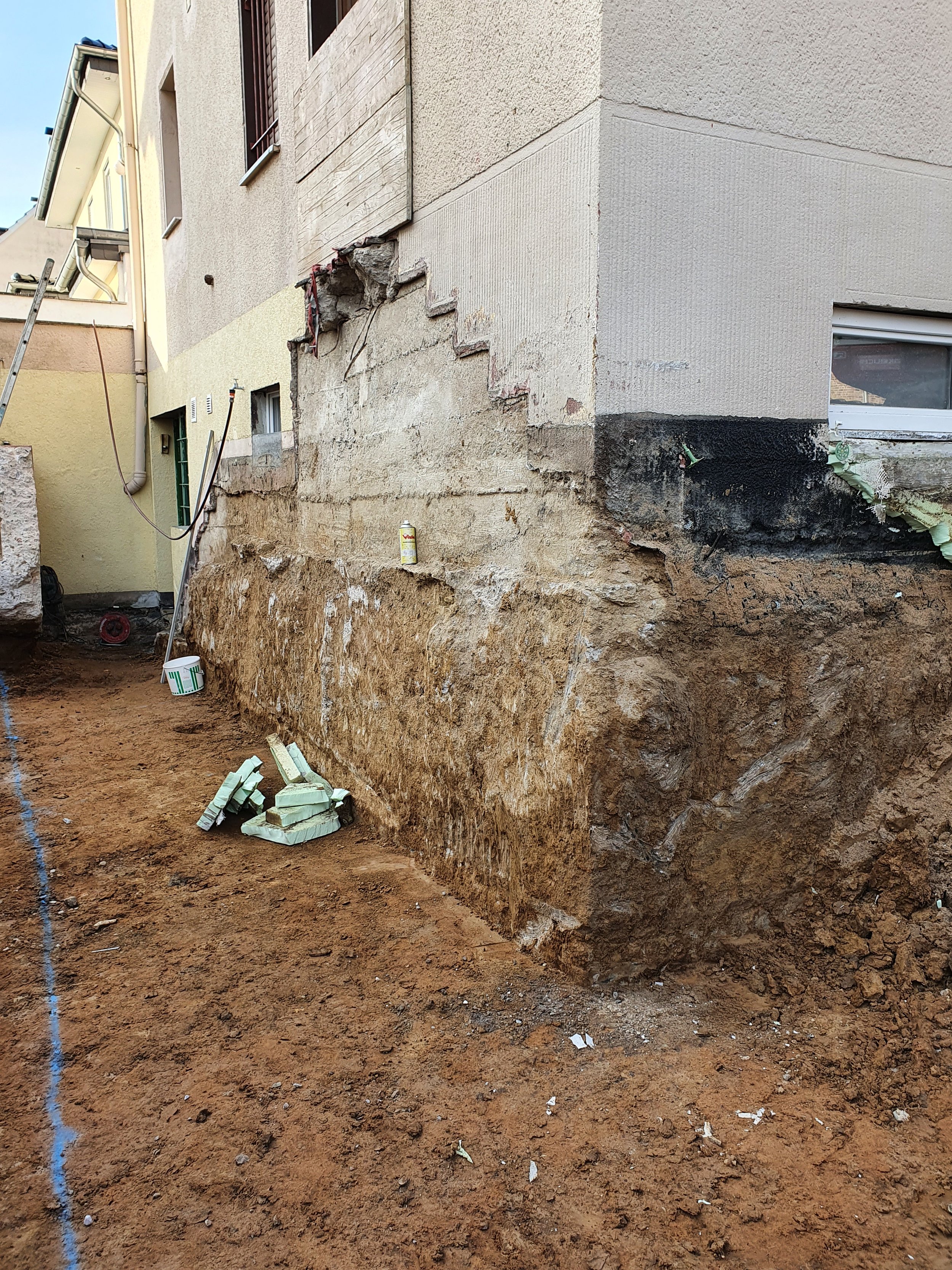 Ausgegrabener Baugrund neben einem Haus mit sichtbarer Außenwand, die repariert wird.