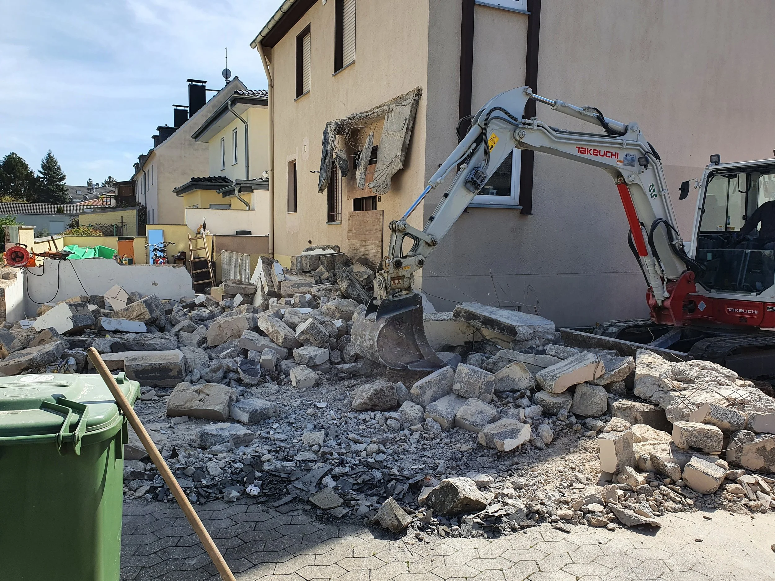Abbruch eines Hauses mit Bagger auf einem schmutzigen Schneideplatz vor Wohnhäusern in einer ruhigen Nachbarschaft.