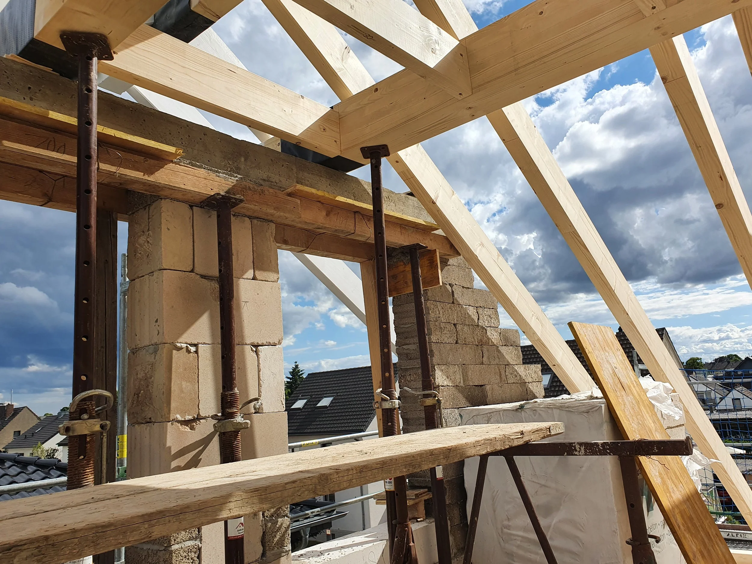 Robin in construction helmet in the foreground, building construction with bricks and wooden framework, sky with clouds in the background.