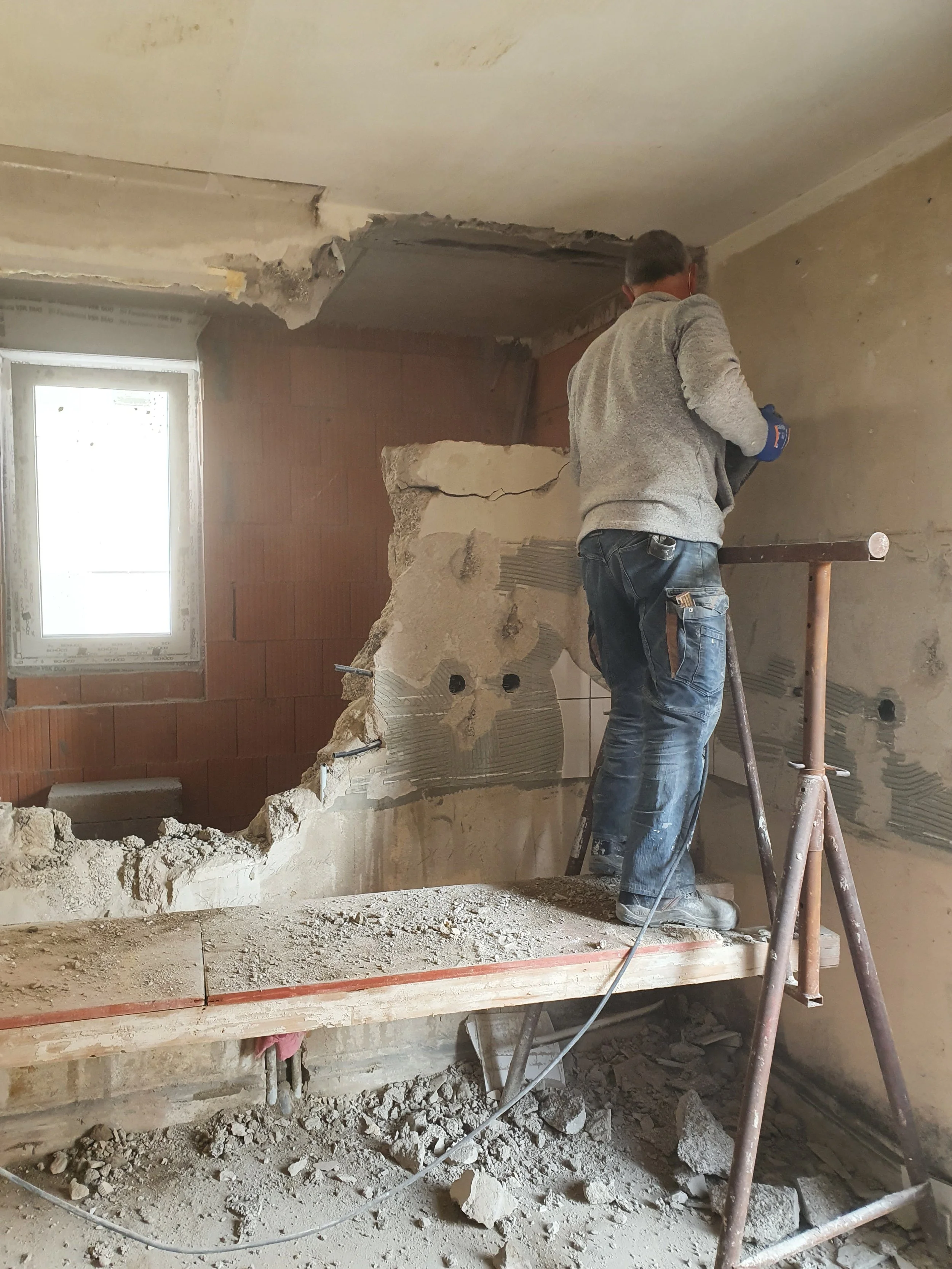 Ein Handwerker entfernt eine Wand in einem Raum unter Umbauarbeiten.