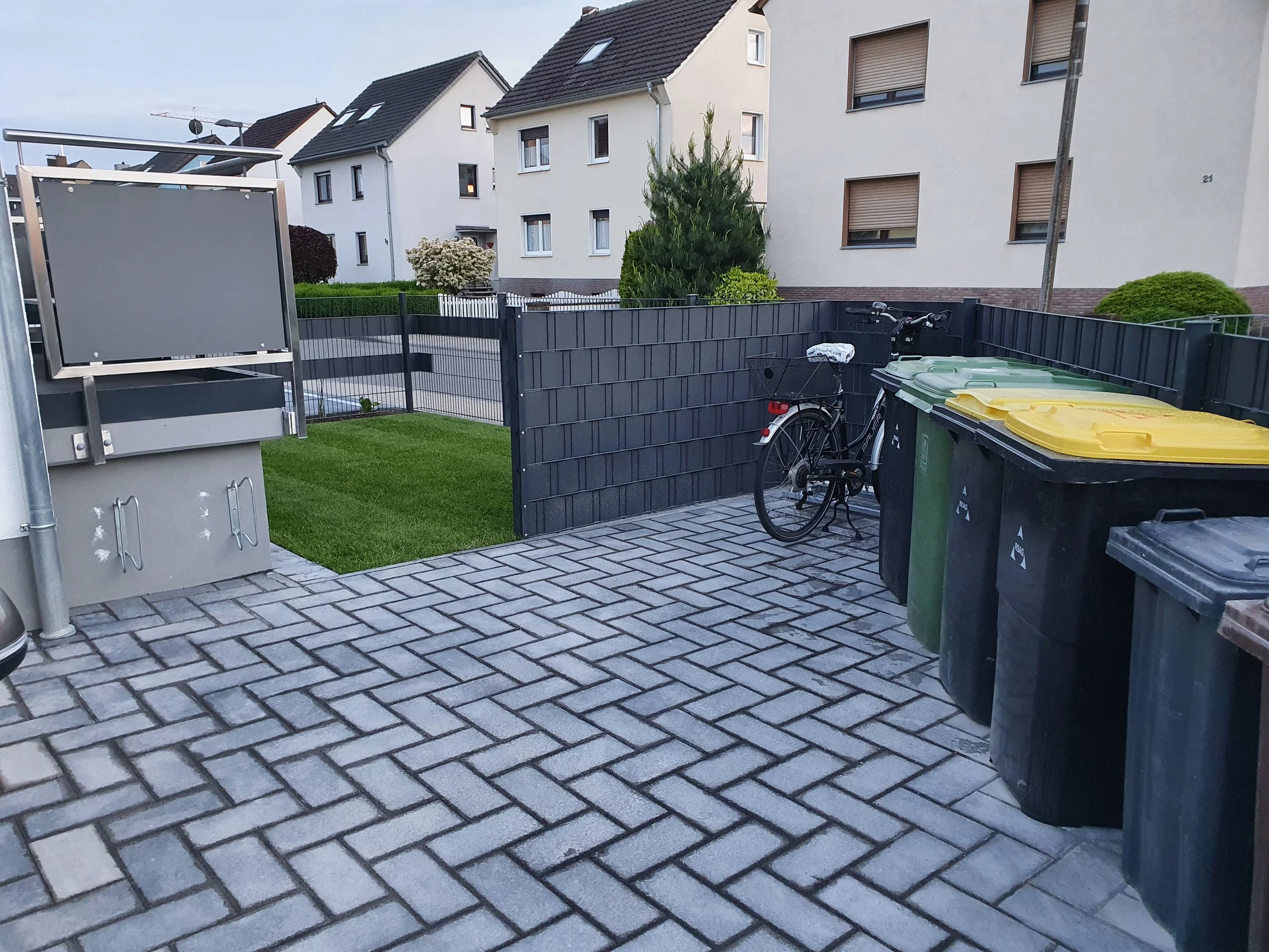 Abfallbehälter und Fahrrad in einem Hof vor einem weißen Mehrfamilienhaus