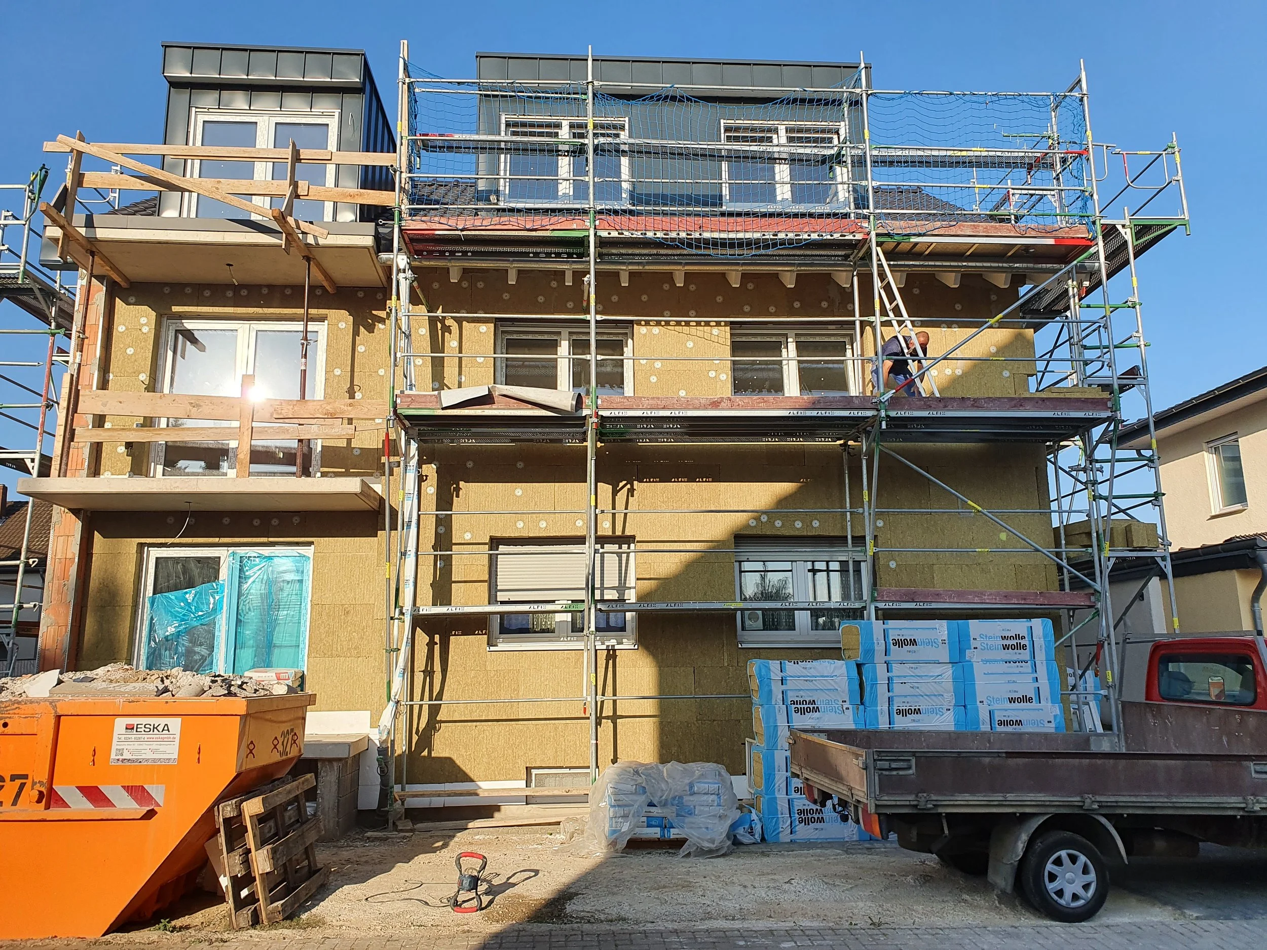 Mehrstöckiges Gebäude im Bau mit Gerüsten und Baumaterialien, Bauarbeiter arbeitet.