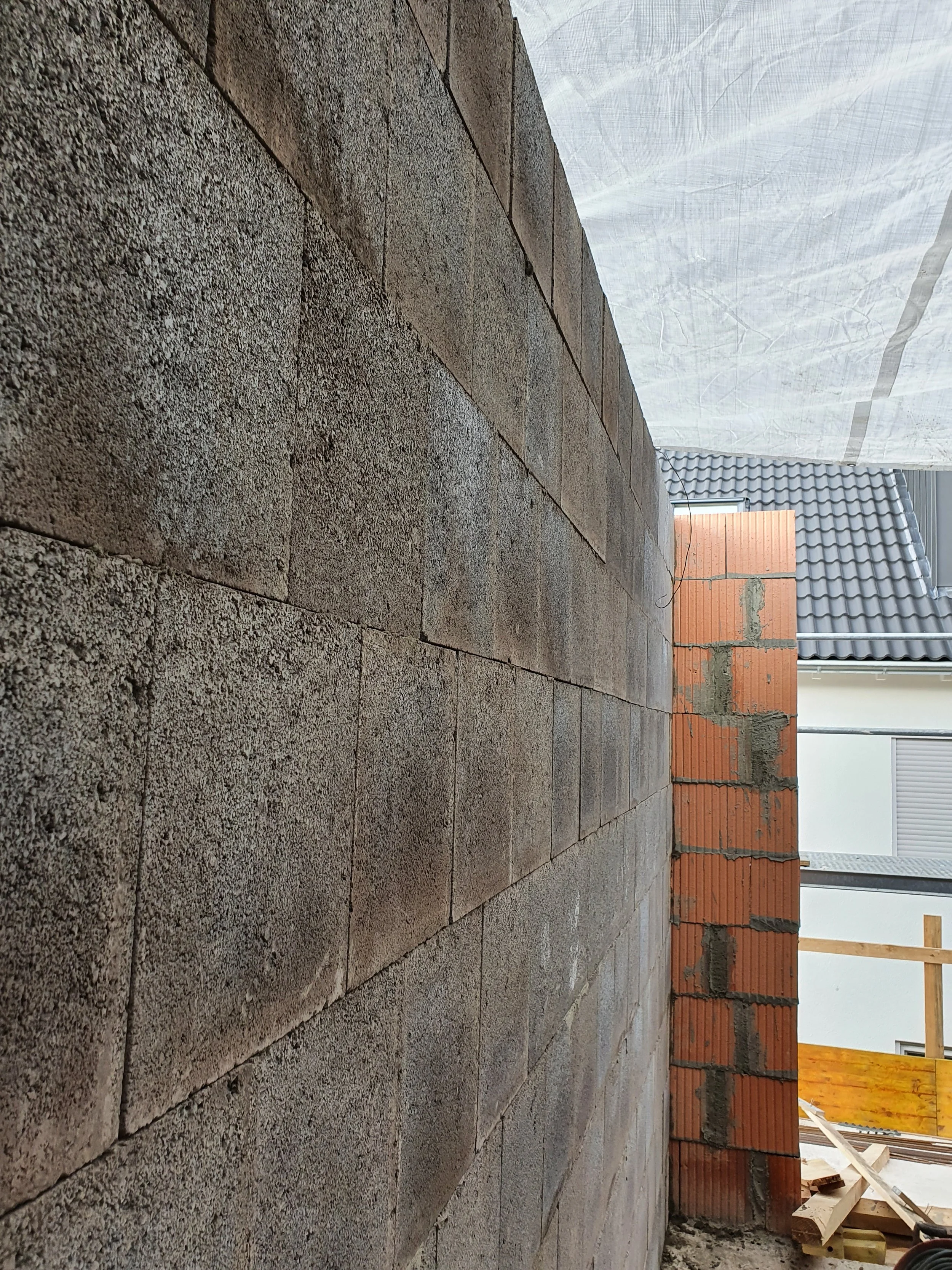Baustelle mit Mauer aus Stein und Ziegel, teilweise mit Mörtel, im Hintergrund Baugerüst und Dach mit Ziegeln.