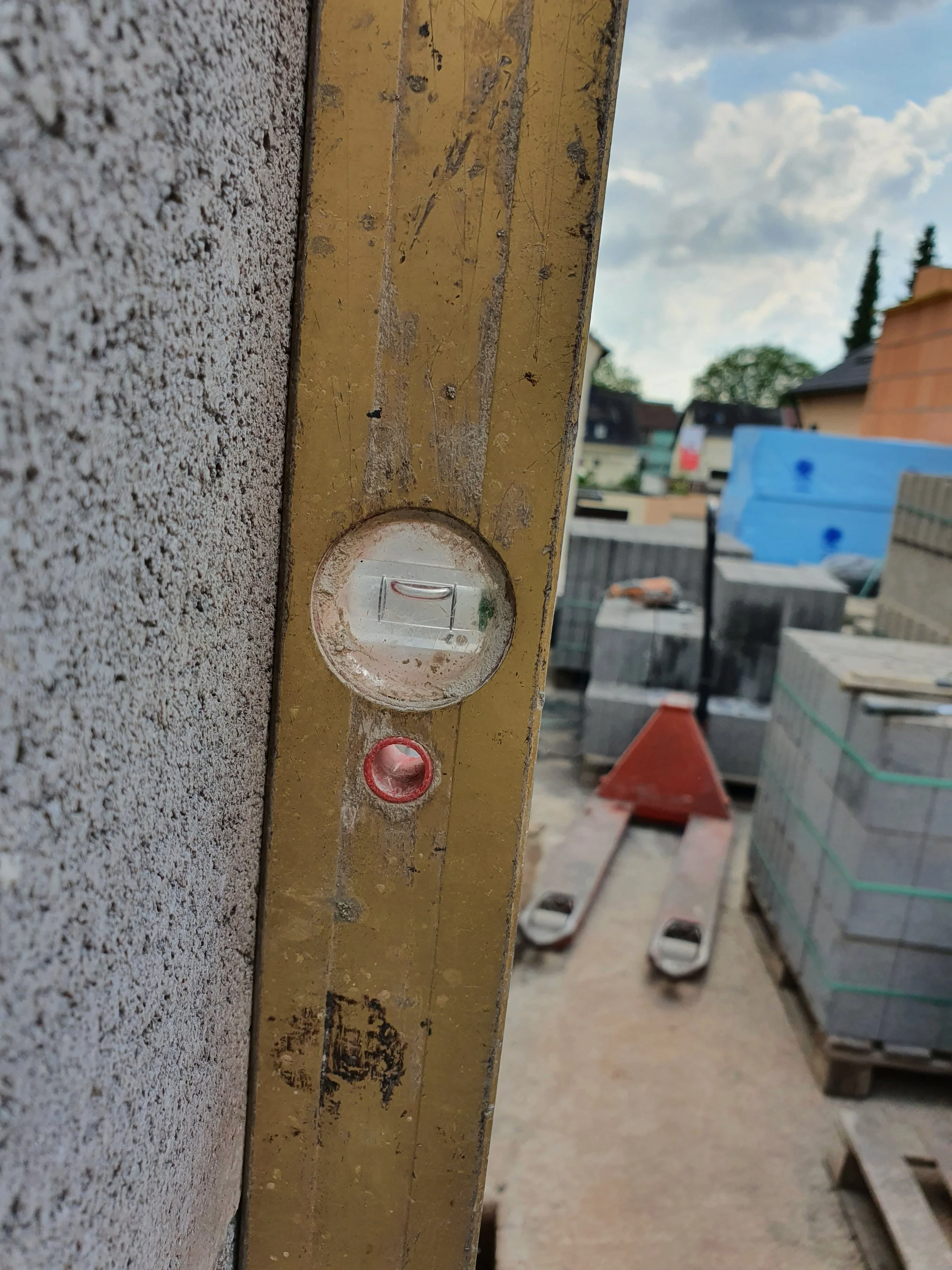 Naheaufnahme einer Wasserwaage an einer Baustelle, im Hintergrund Baumaterialien und eine Baustellenumgebung sichtbar.