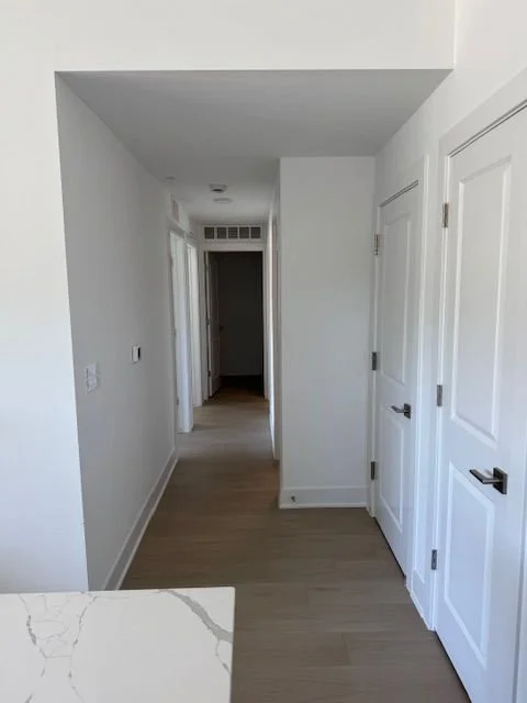 Empty white hallway with doors on the right and a wood floor.