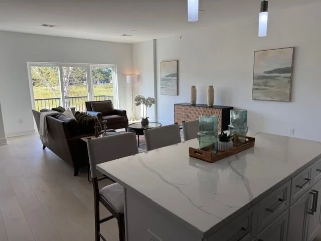 Open-concept living room and kitchen with large windows, gray and white decor, and modern furniture.