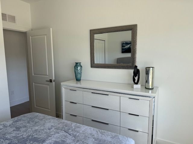 A white dresser with eight drawers, topped with two vases and decorative objects, a wall mirror, and a doorway in a bedroom with white walls.