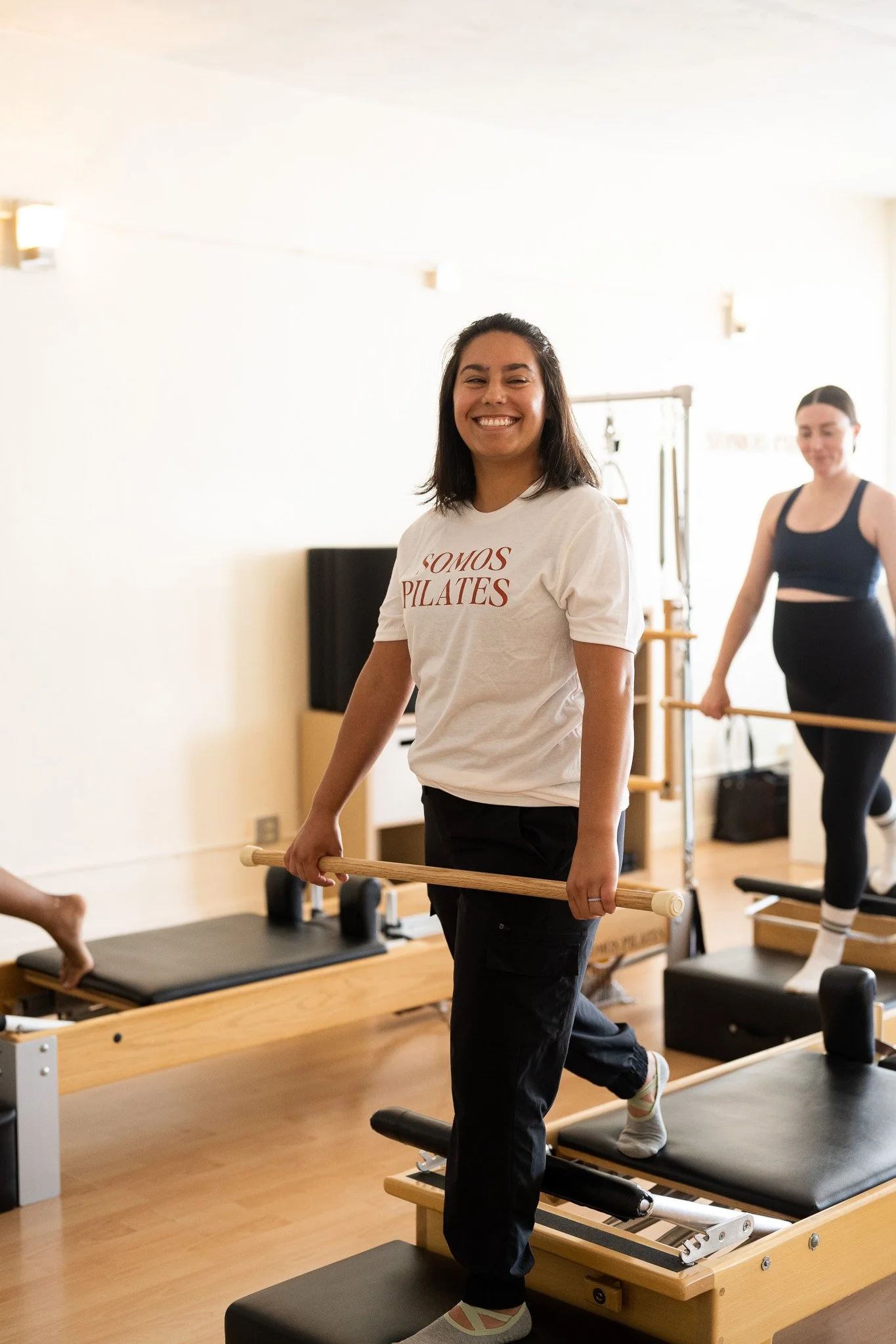 Client doing reformer Pilates with a wooden dowel at Somos Pilates studio in Albuquerque