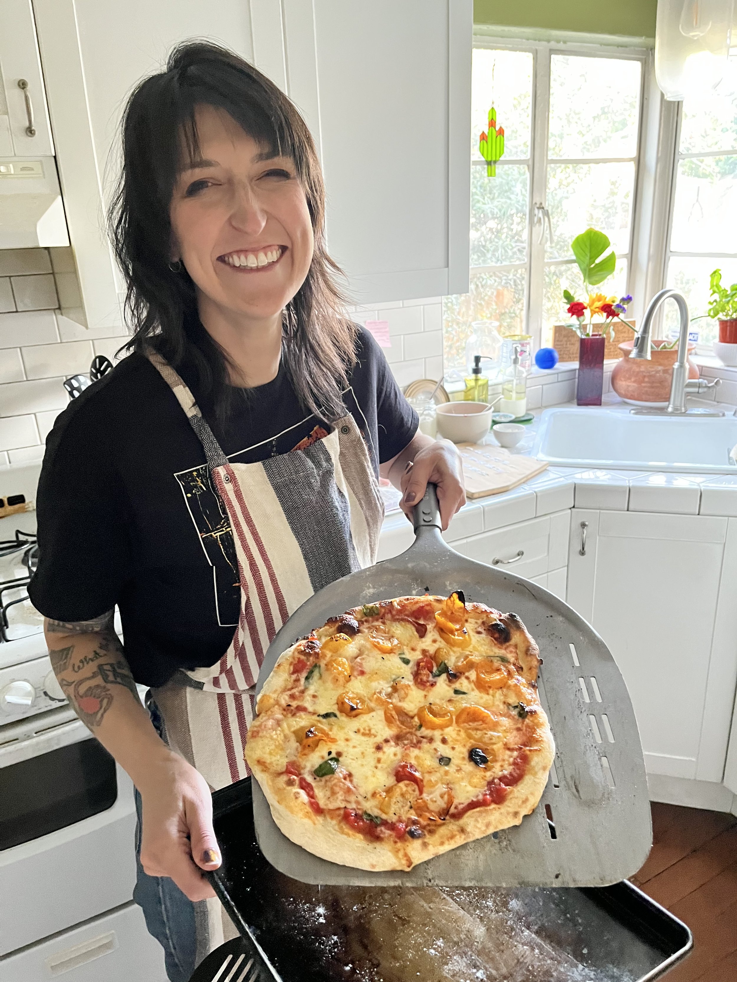 Brittany Feenstra holding up a pizza she made in a kitchen