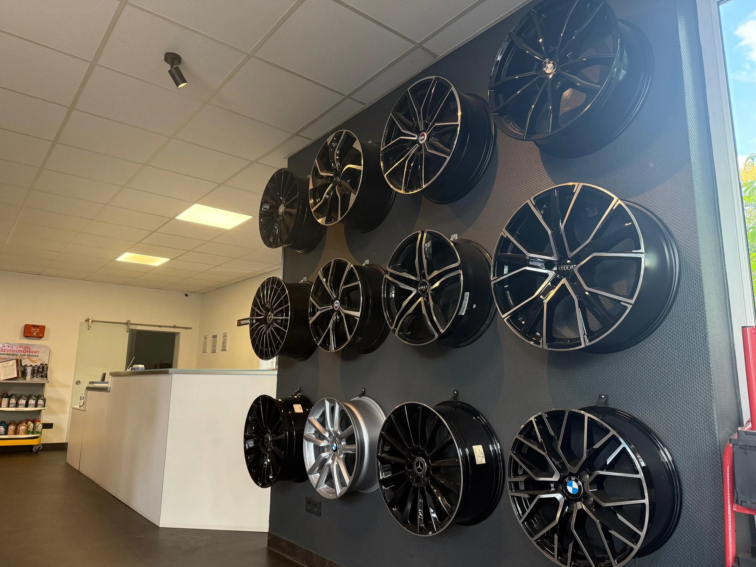 Autofelgen verschiedener Designs und Marken, montiert auf einer schwarzen Wandfläche in einem Autozubehörgeschäft.