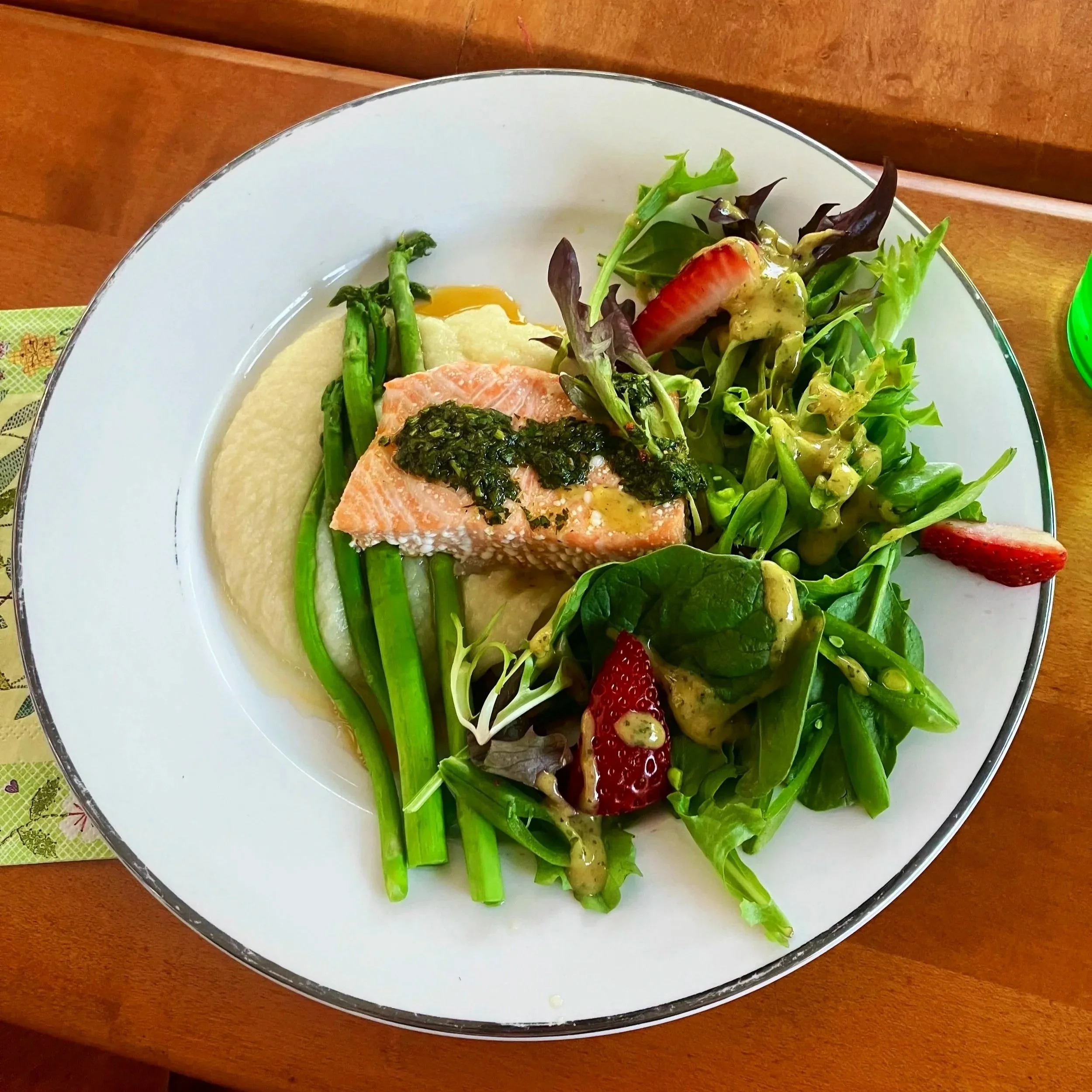 Plate with salmon, mashed potatoes, green beans, mixed greens, strawberries, and avocado slices.