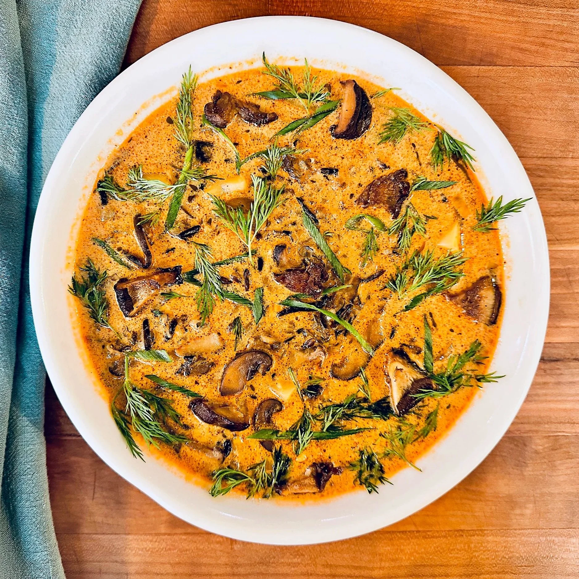 A bowl of creamy mushroom soup garnished with fresh herbs on a wooden table.