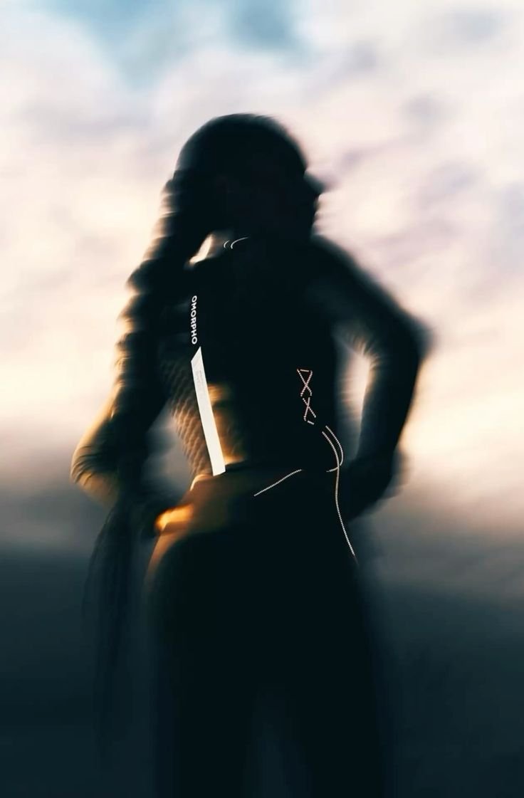 A blurry silhouette of a woman standing outdoors with her hand on her hip, in front of a cloudy sky, wearing a fitted outfit with a visible tag or label on the side.