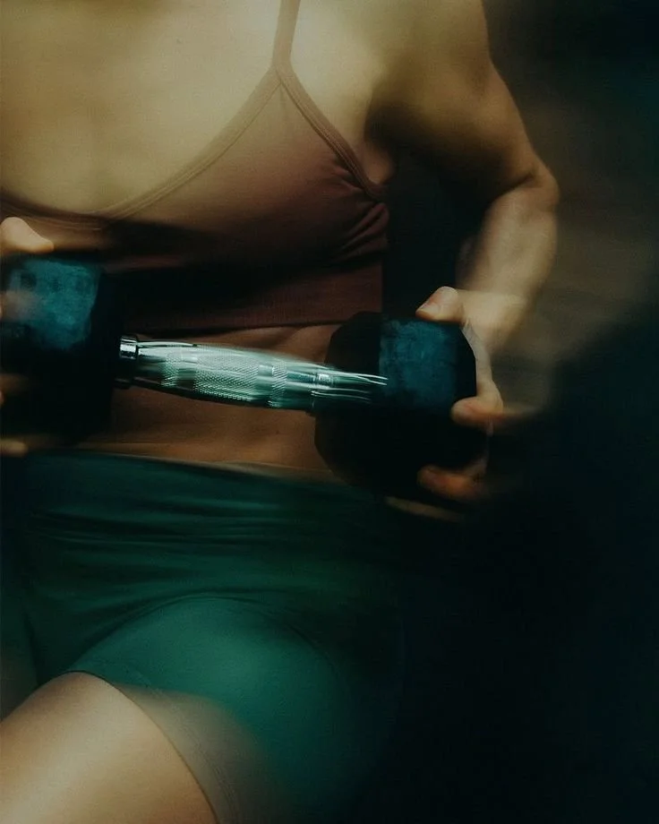 Close-up of a woman lifting a dumbbell in a gym, wearing a sports bra and shorts.