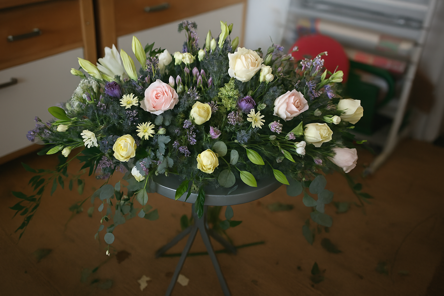 A large floral arrangement with white, pink, and purple flowers on a metal stand, placed on a wooden floor indoors.