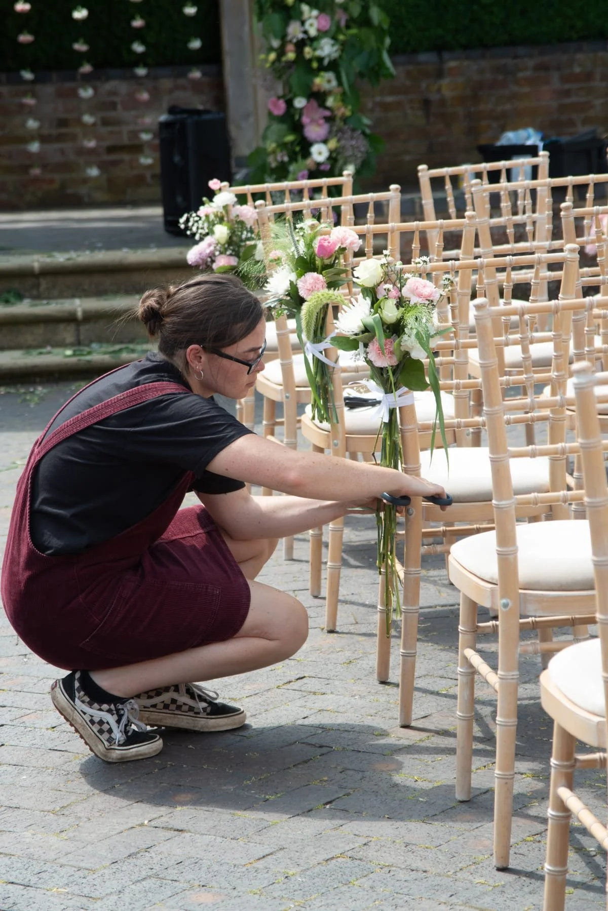 A woman arranging flower bouquets on a chair in an outdoor setting for a wedding or event.